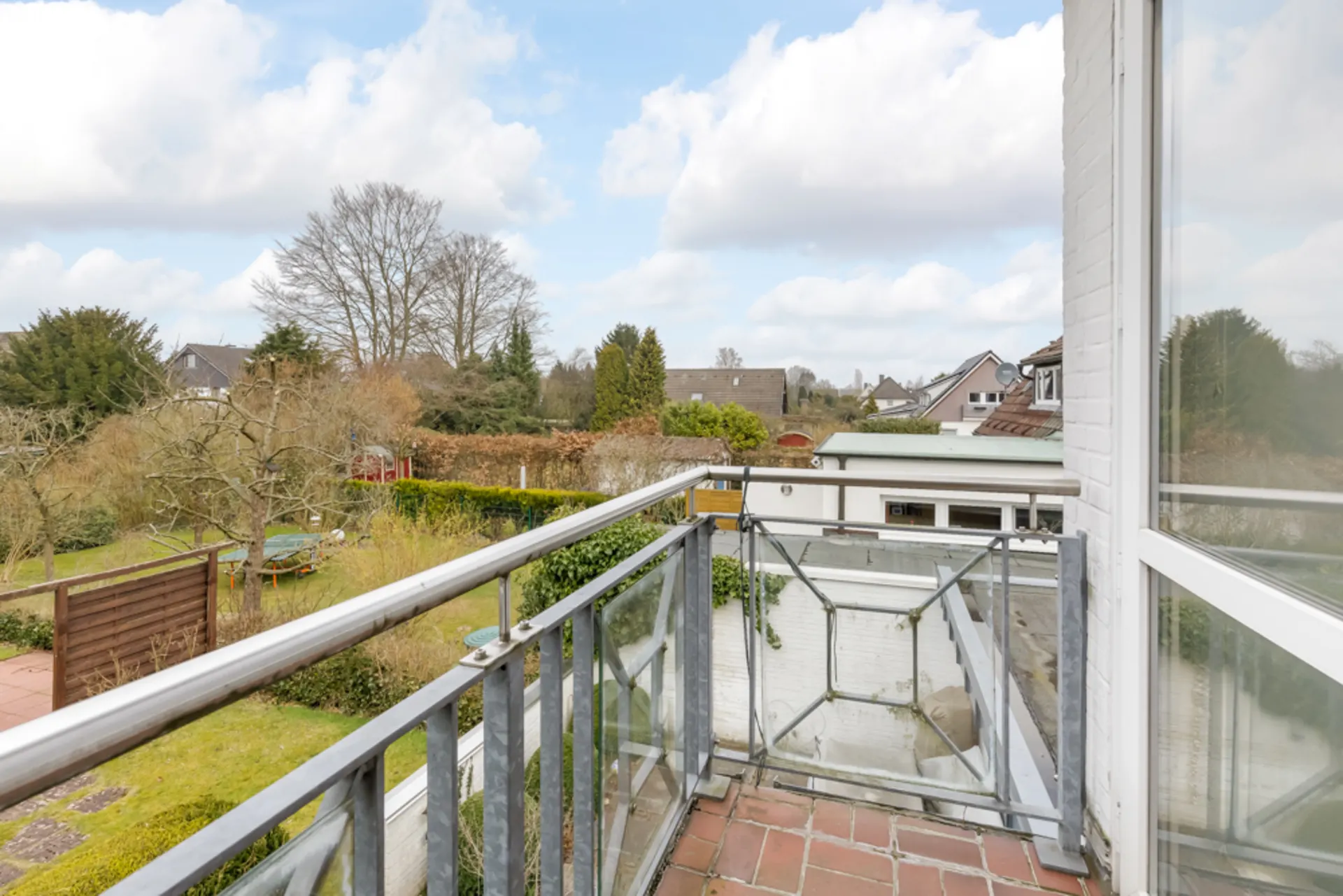 Blick von einem Balkon mit Metallgeländer auf einen Garten und benachbarte Häuser.