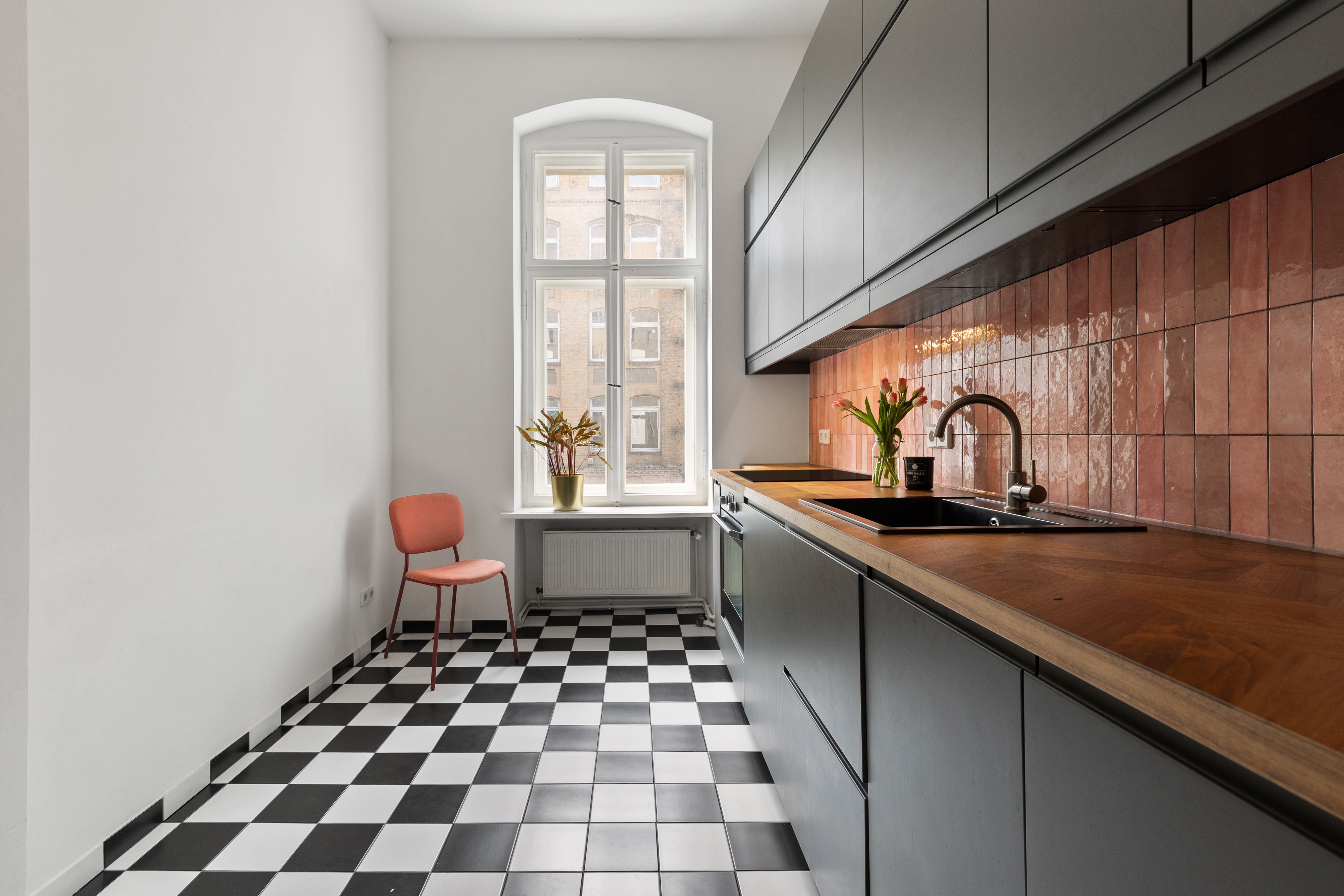 Moderne Küche mit schwarz-weißem Fliesenboden, Holztisch, Spüle und großem Fenster.