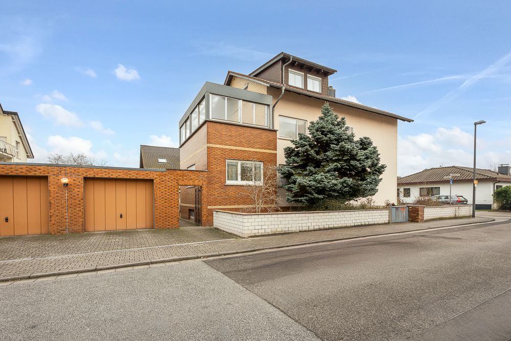 Modernes Wohnhaus mit drei Etagen, Ziegelgarage und Nadelbaum an einer Straßenecke.