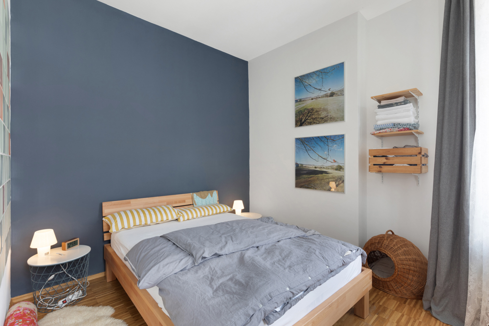 Modernes Schlafzimmer mit Holzbett, blauer Akzentwand, Nachttischen und Wandbildern.