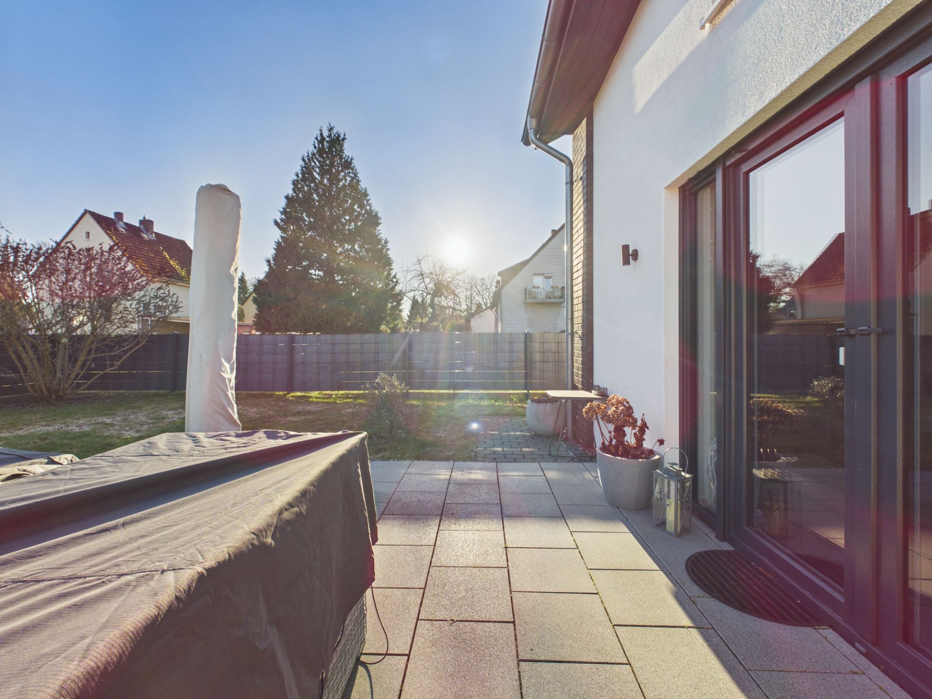 Sonnige Terrasse mit Fliesen, Pflanzenkübeln und Blick auf Garten und Nachbarhäuser.