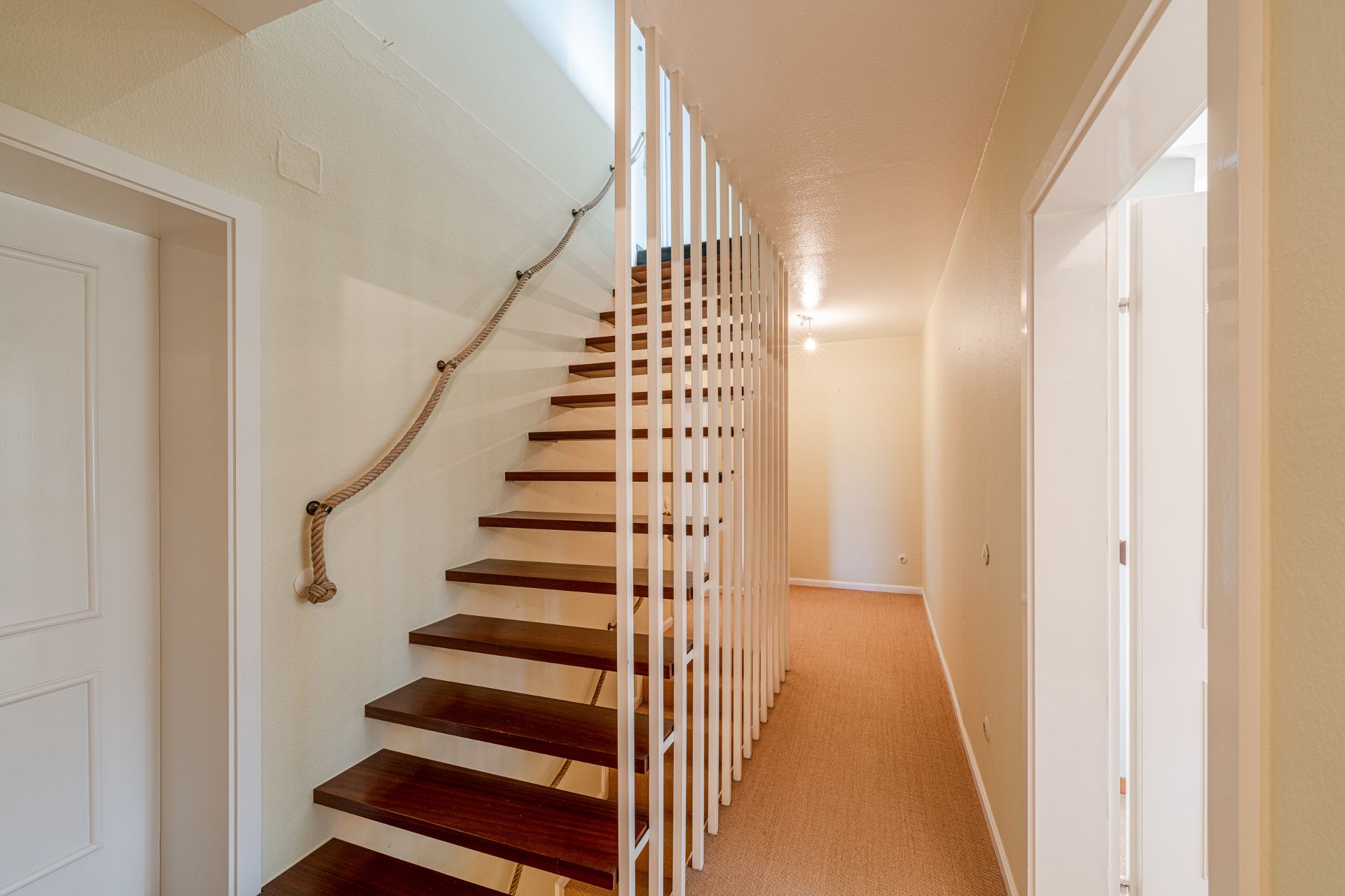 Moderne Holztreppe mit Seilgeländer und weißem Geländer in einem Flur.
