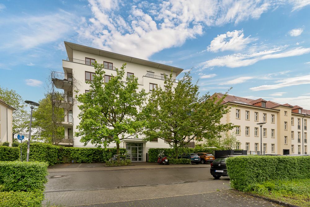 Modernes Wohngebäude mit mehreren Stockwerken, Bäumen davor und Autos auf dem Parkplatz.