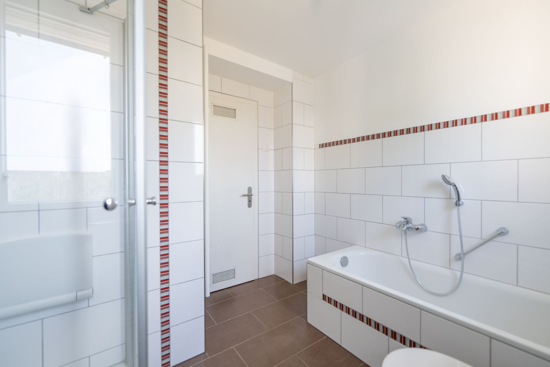 Modernes Bad mit Badewanne, Dusche, weißen Fliesen und braunem Boden.