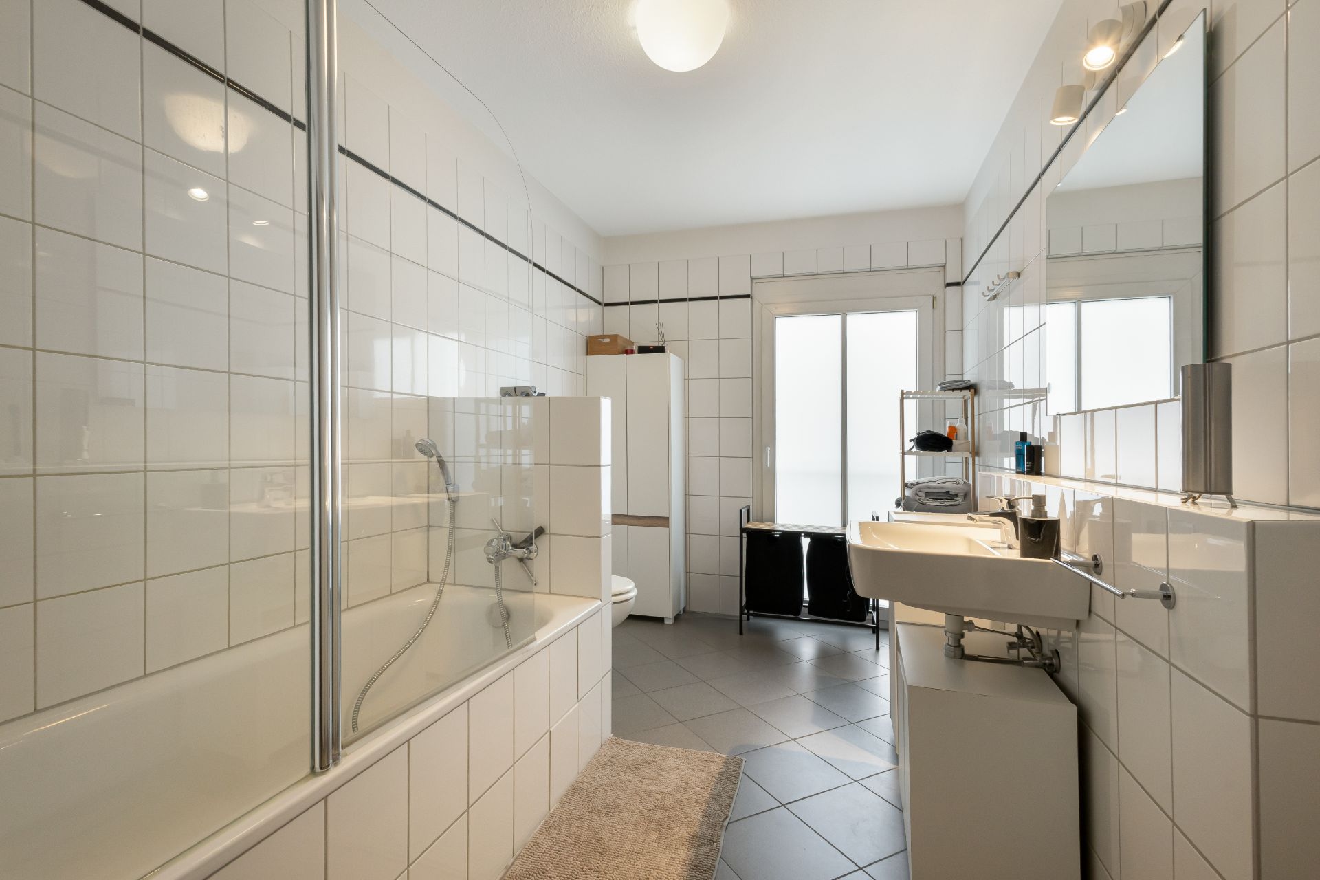 Modernes Badezimmer mit Badewanne, Waschbecken, Spiegel und weißen Fliesen.