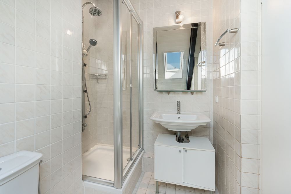 Helles Badezimmer mit Dusche, Waschbecken, Spiegel und weißen Fliesen.