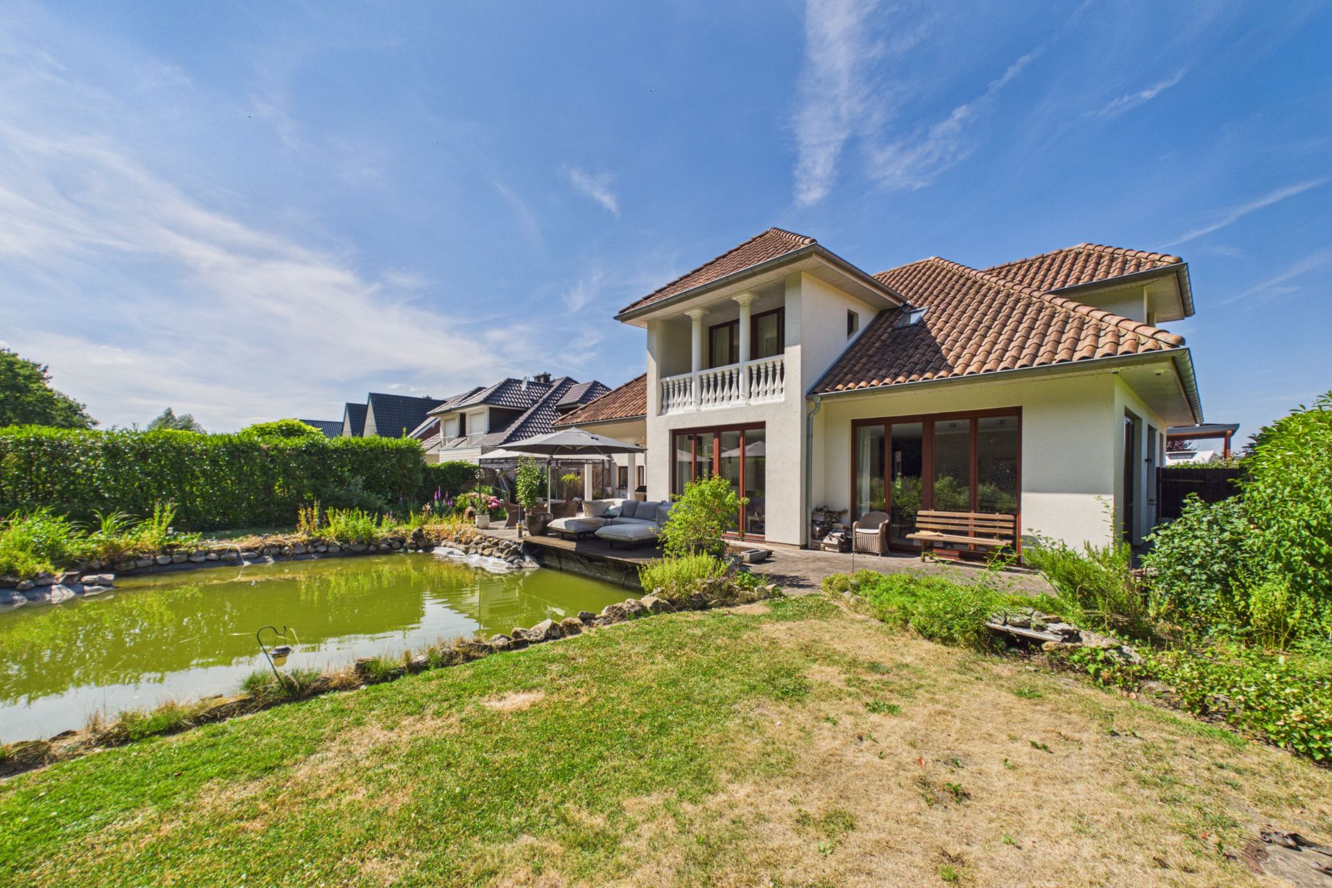 Modernes Wohnhaus mit großem Garten und Teich unter blauem Himmel.