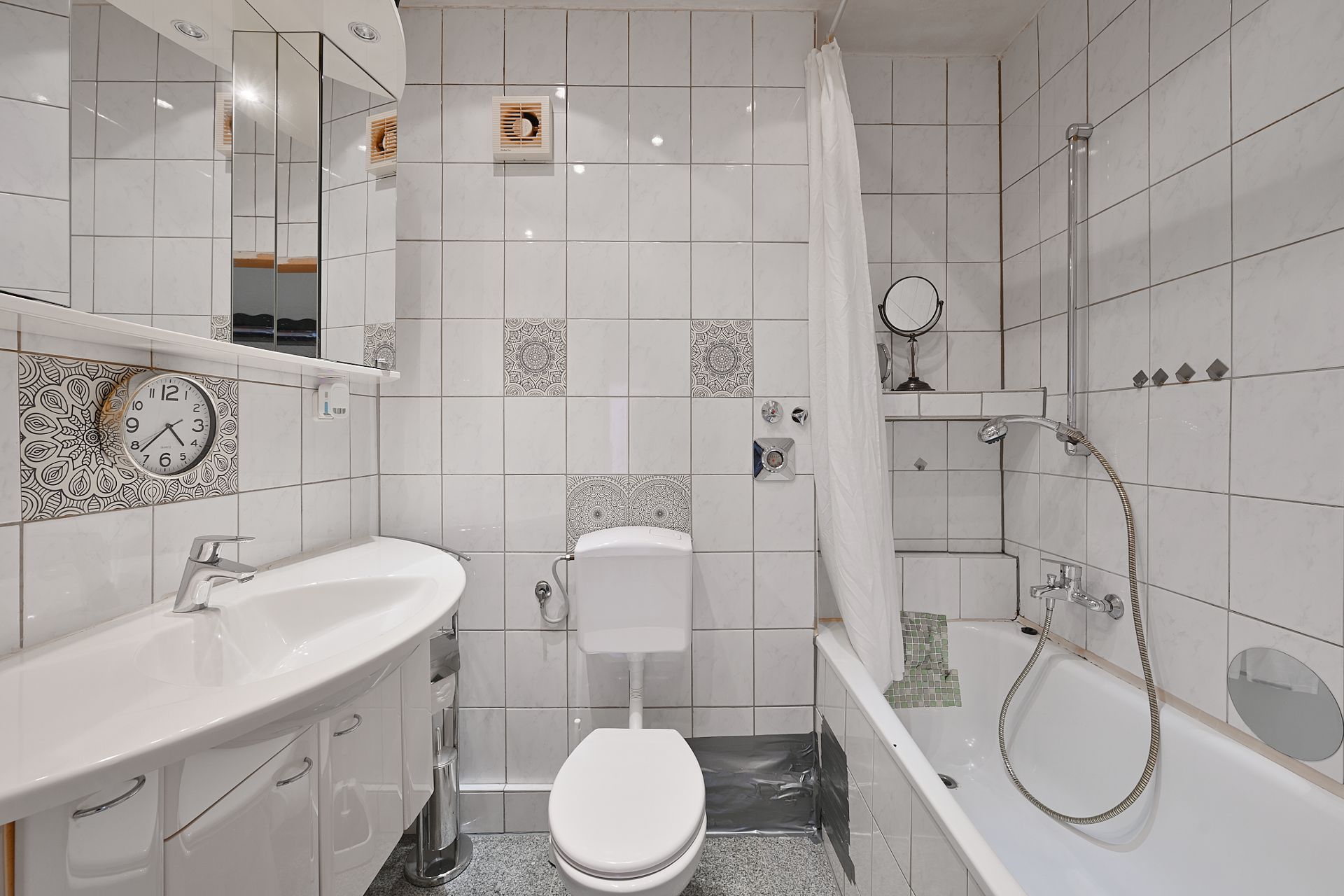 Helles Badezimmer mit Waschbecken, Spiegel, Toilette und Badewanne mit Duschvorhang.