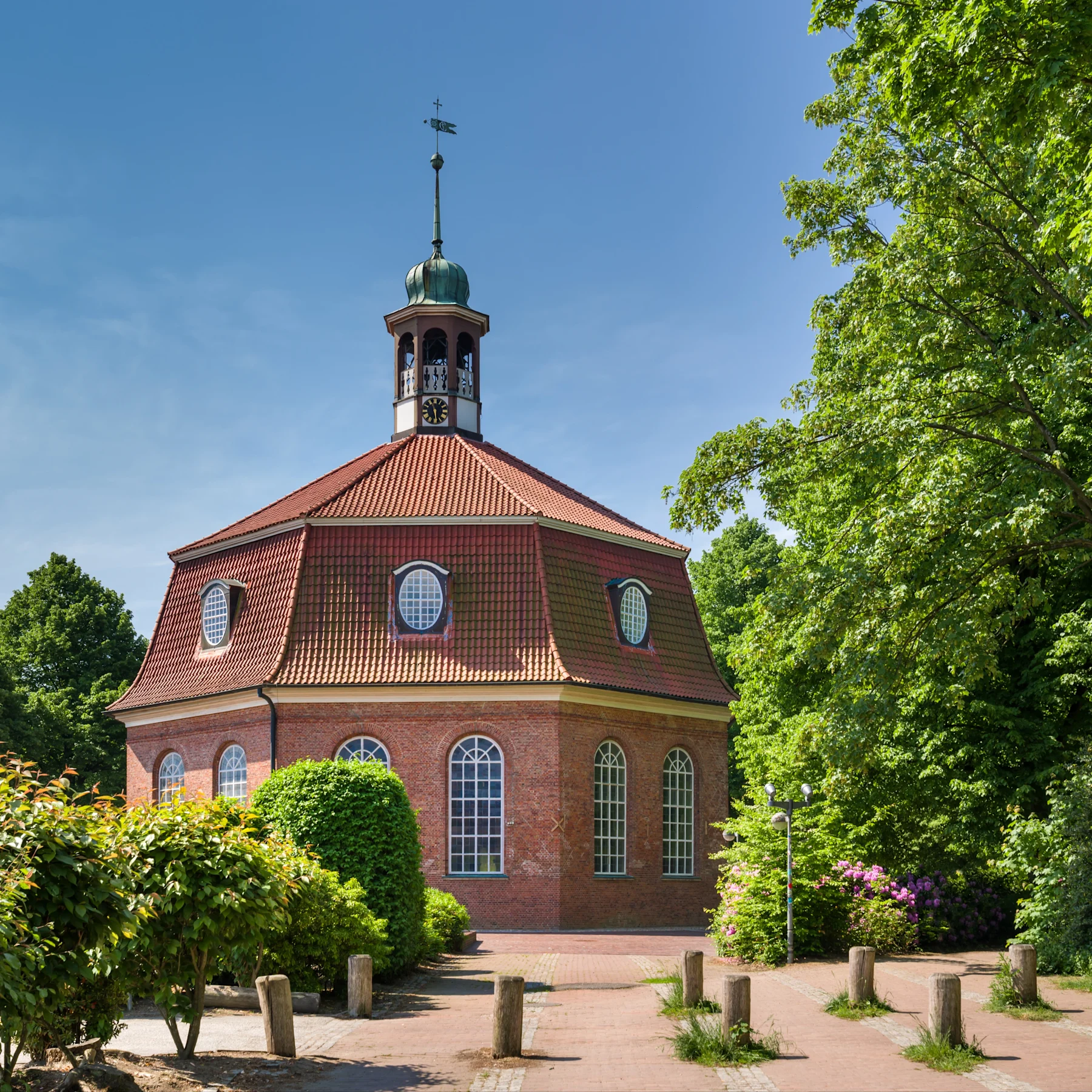Backstein-Gebäude mit achteckigem Turm und großen Fenstern, umgeben von Bäumen.