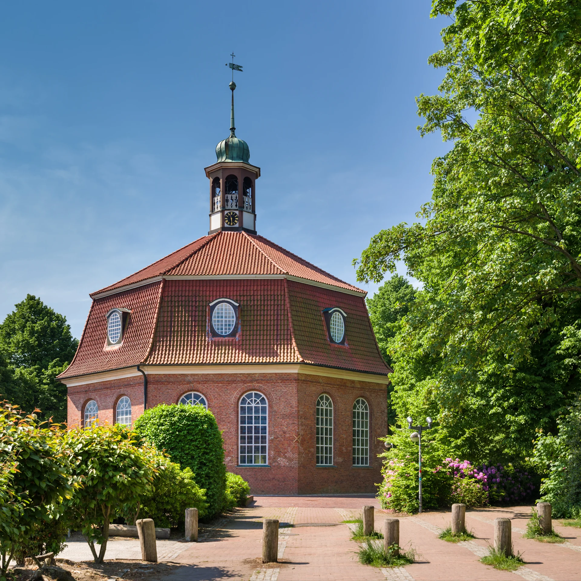 Backstein-Gebäude mit achteckigem Turm und großen Fenstern, umgeben von Bäumen.