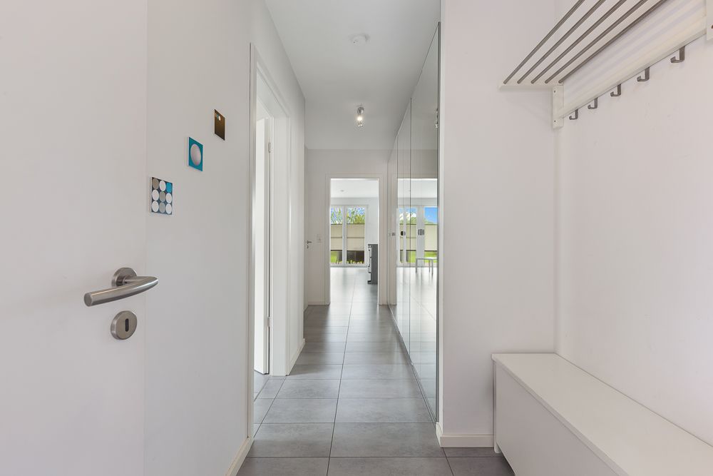 Heller Flur mit Fliesenboden, Garderobe und Sitzbank, Spiegel an der rechten Wand.