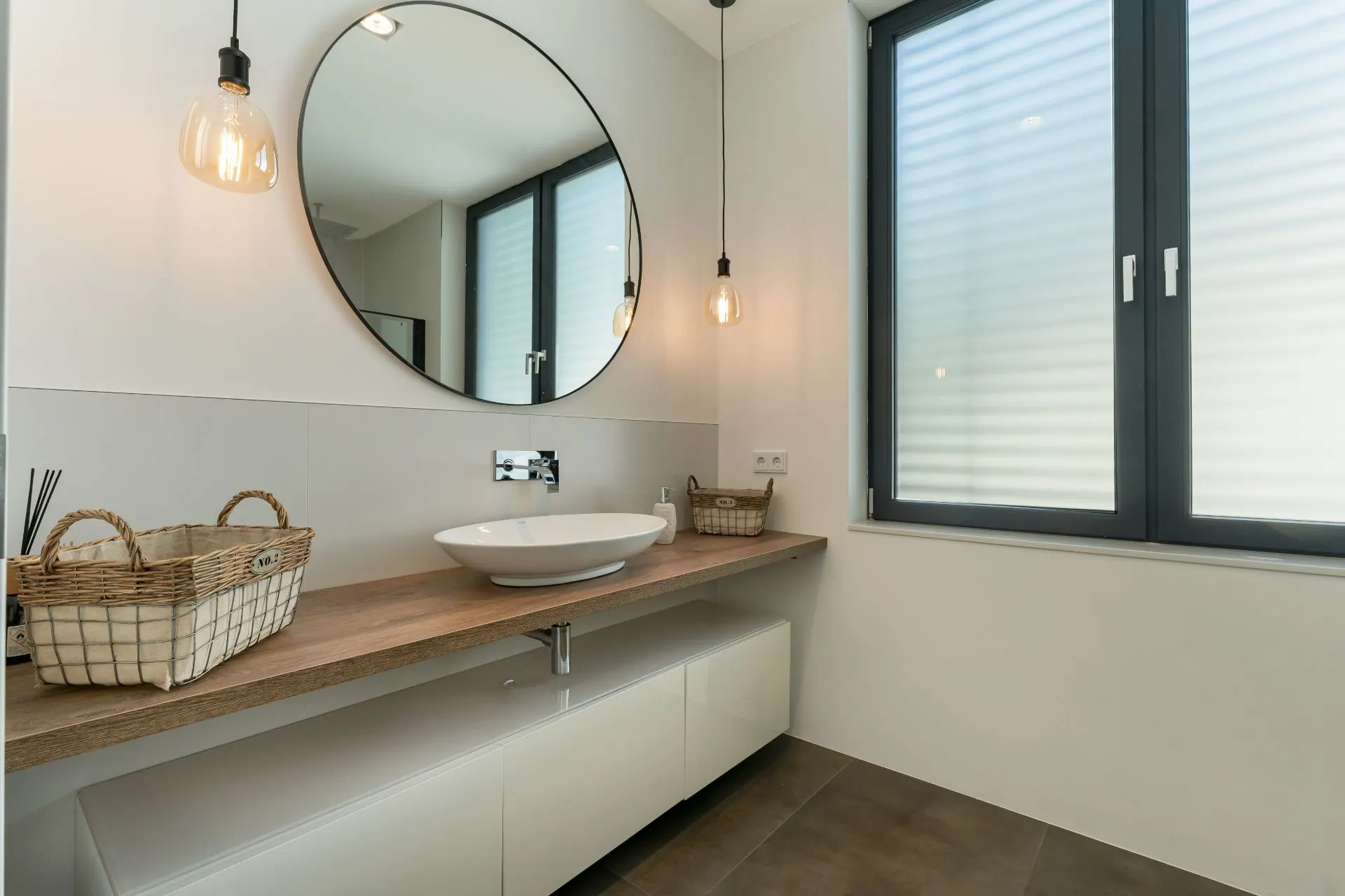 Modernes Badezimmer mit großem Spiegel, Waschbecken, Holztisch und zwei Körben am Fenster.