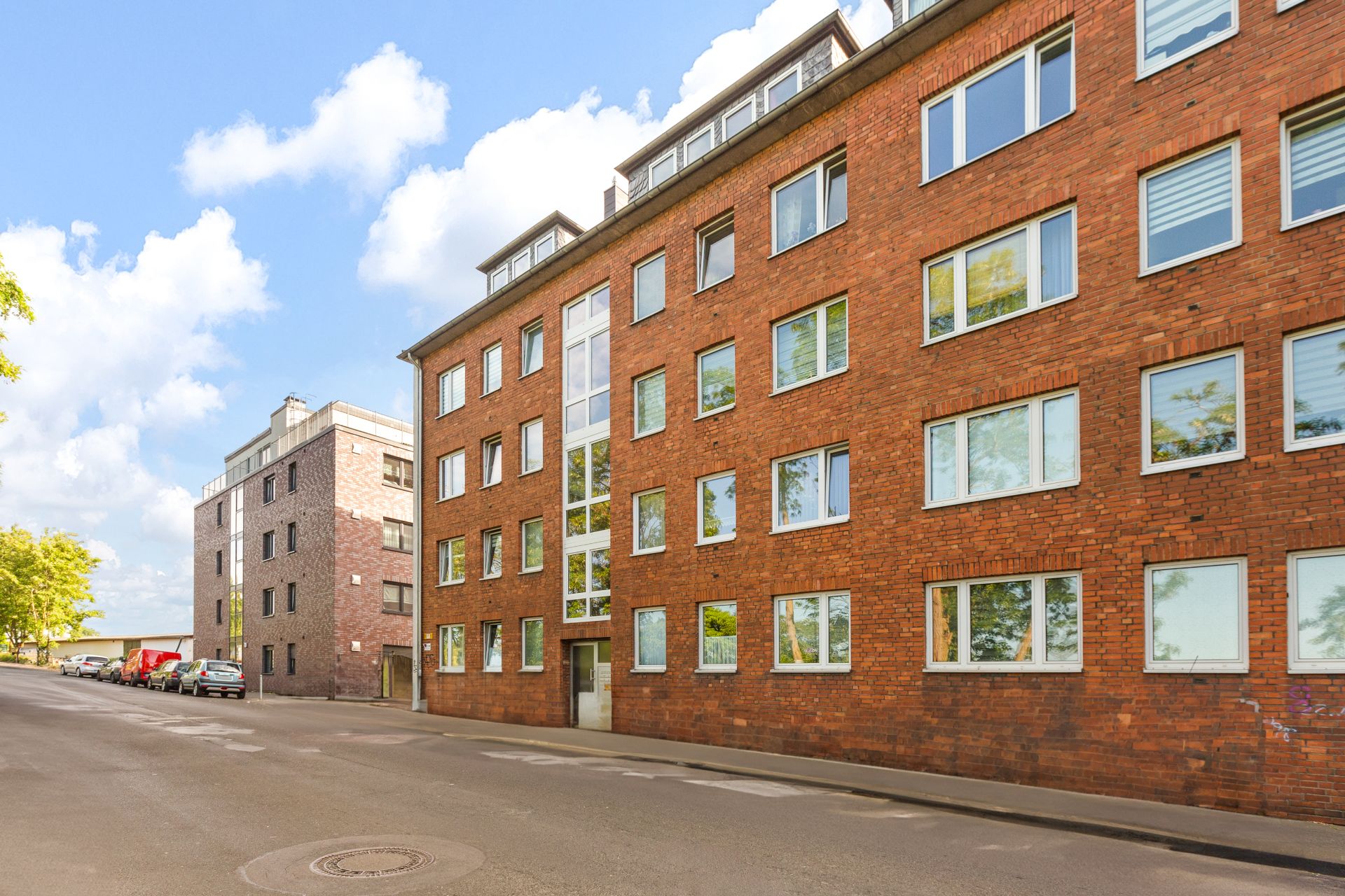 Mehrstöckiges Wohnhaus aus rotem Backstein mit vielen Fenstern an einer ruhigen Straße.
