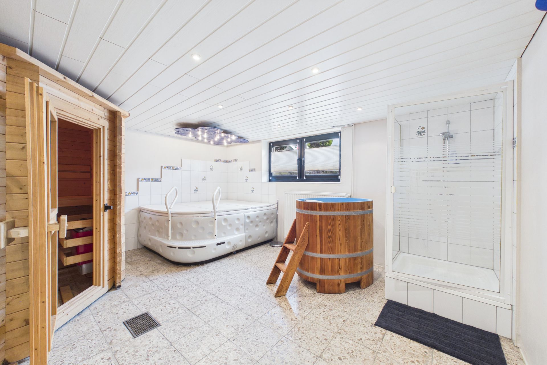 Wellnessraum mit Sauna, Whirlpool, Holzbottich und Dusche, Fenster an der Wand.