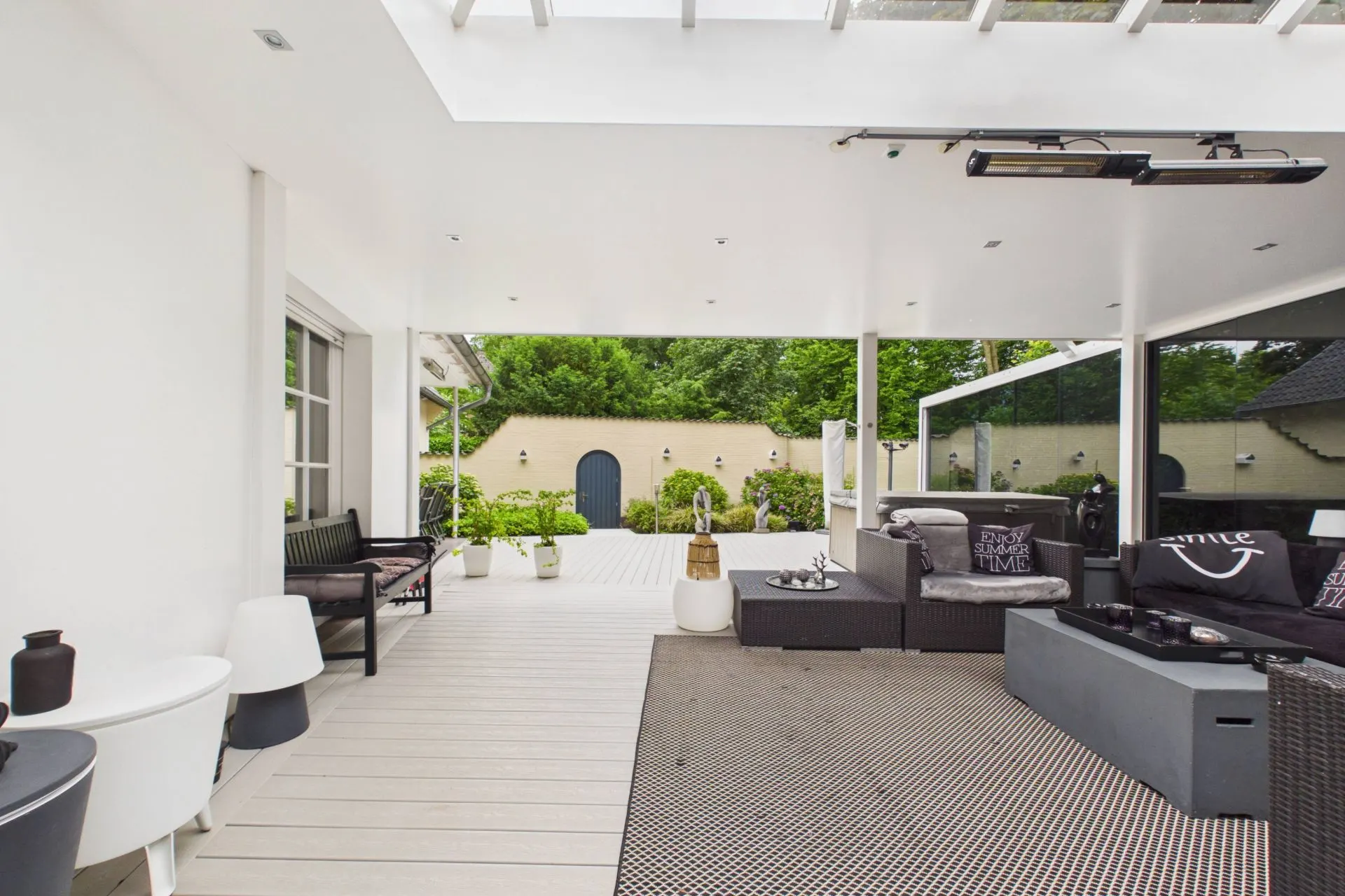 Überdachte Terrasse mit Sitzbereich, weißen Wänden und Blick auf Garten mit Pflanzen.