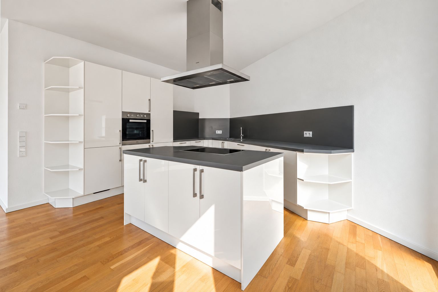 Moderne weiße Einbauküche mit Kochinsel und dunkler Arbeitsplatte auf Holzboden.