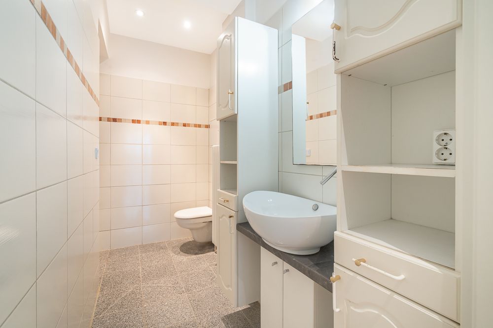 Helles Badezimmer mit Waschbecken, offenen Regalen und WC, gefliest und gut beleuchtet.