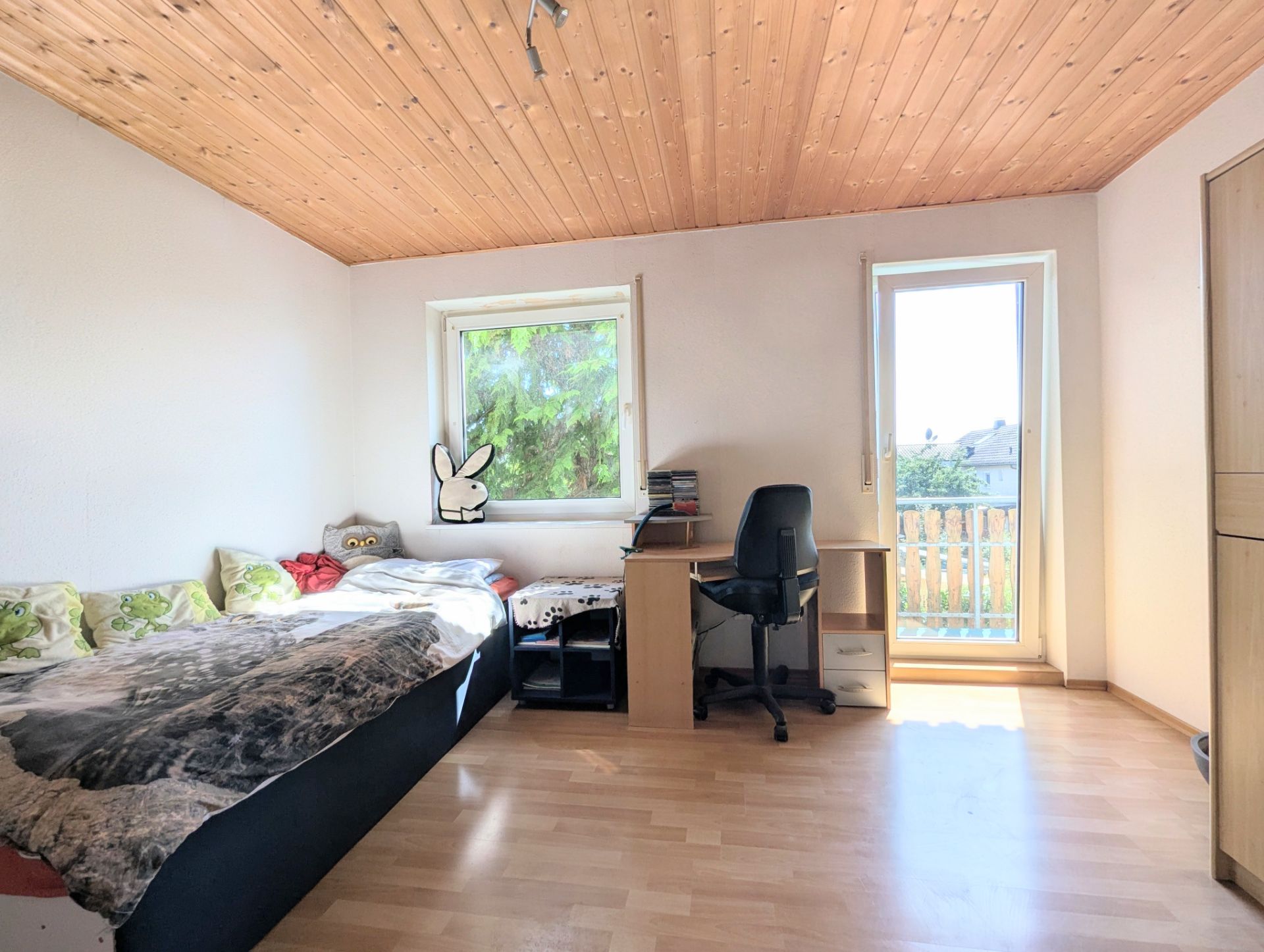 Helles Schlafzimmer mit Bett, Schreibtisch, Stuhl und Zugang zu einem Balkon.