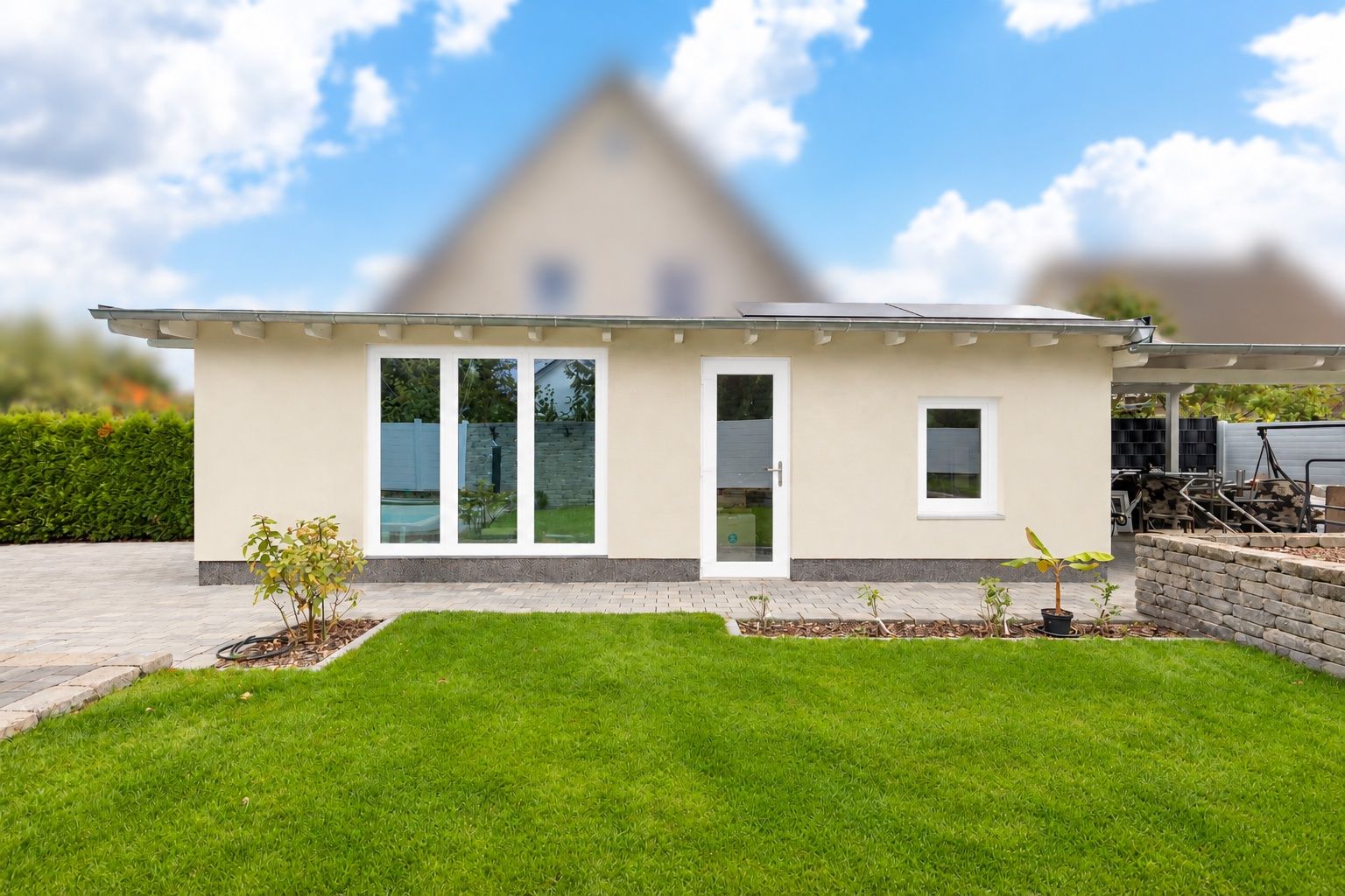 Kleines, einstöckiges Haus mit weißer Fassade, großen Fenstern und Garten im Vordergrund.