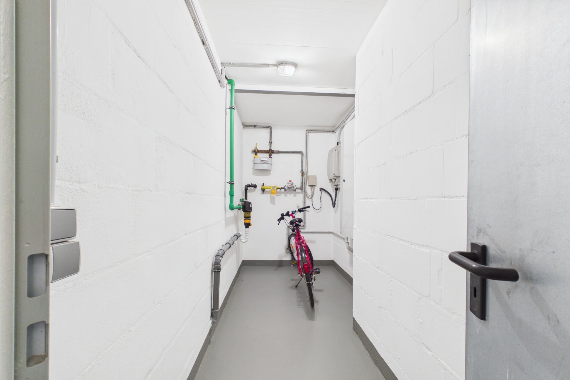 Schmaler, weißer Hauswirtschaftsraum mit Leitungen und einem roten Fahrrad an der Wand.