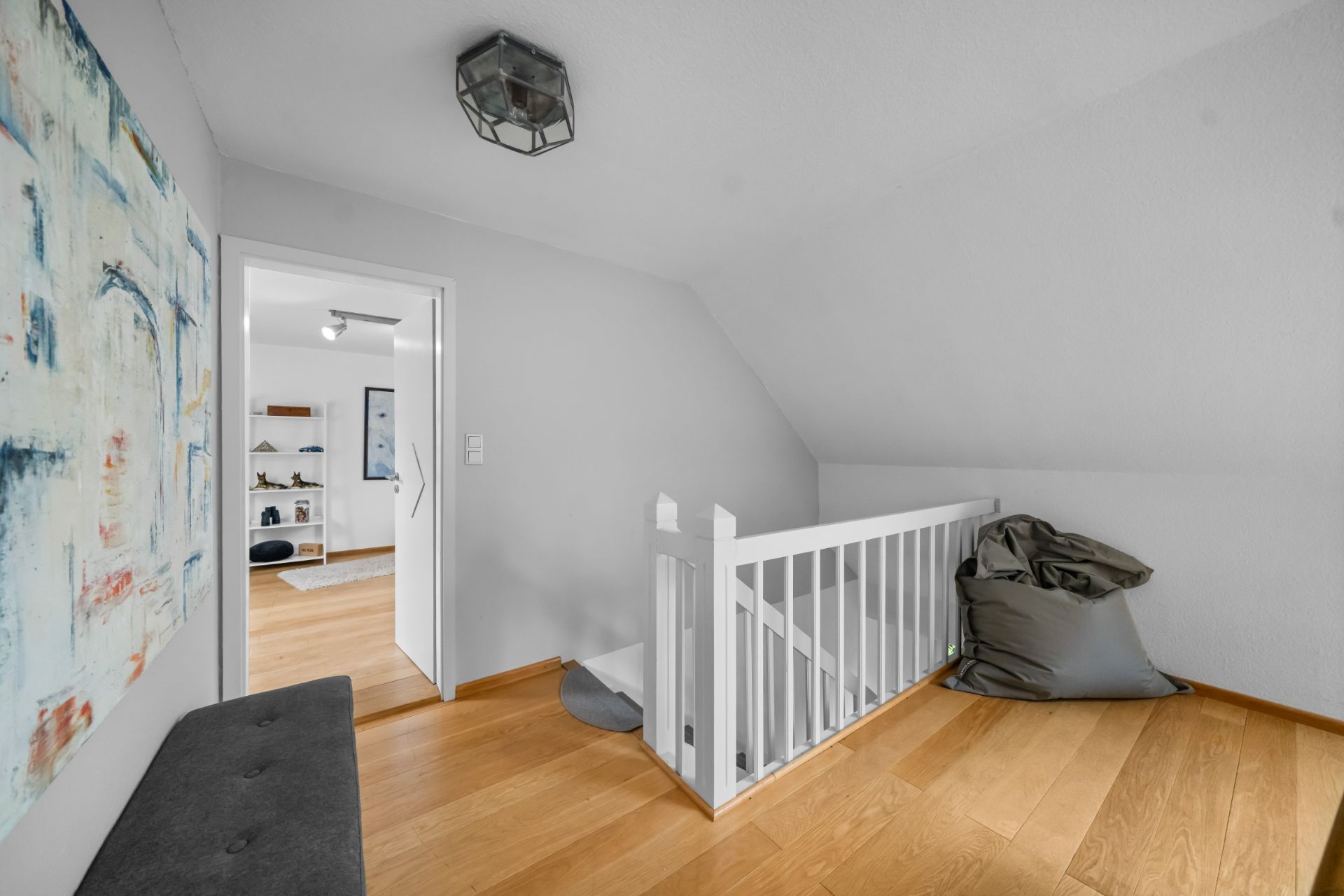 Heller Flur mit Holzfußboden, Treppengeländer, Sitzsack und modernem Wandbild.