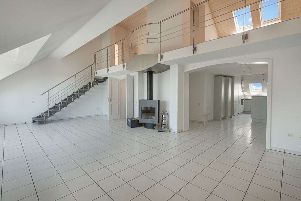 Großes, helles Wohnzimmer mit Kamin, Treppe ins Obergeschoss und offener Küche, Fliesenboden.