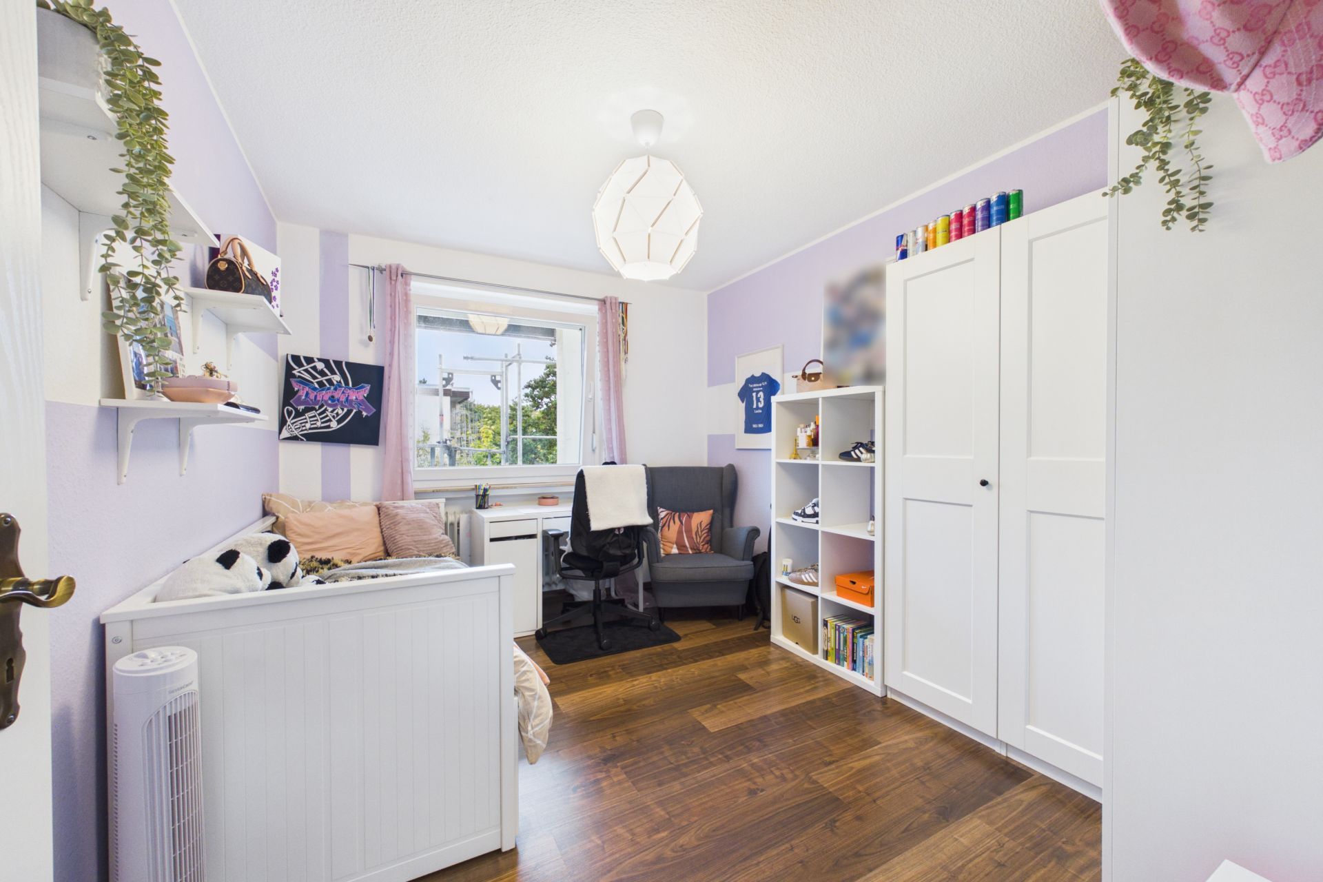 Helles Kinderzimmer mit Bett, Schreibtisch am Fenster, Regal und Kleiderschrank auf Holzfußboden.