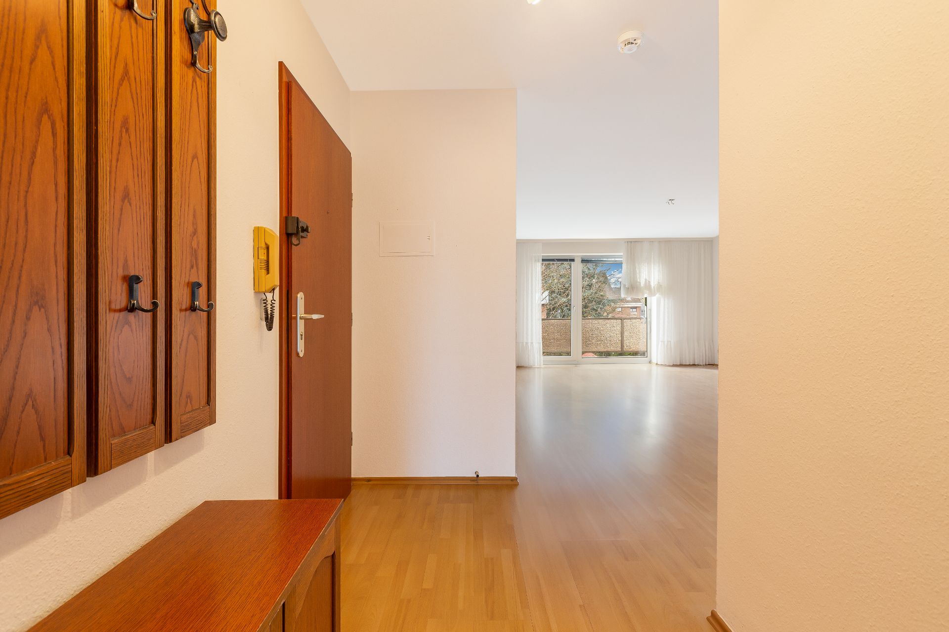 Heller Flur mit Holzmöbeln und Blick ins Wohnzimmer mit großen Fenstern.