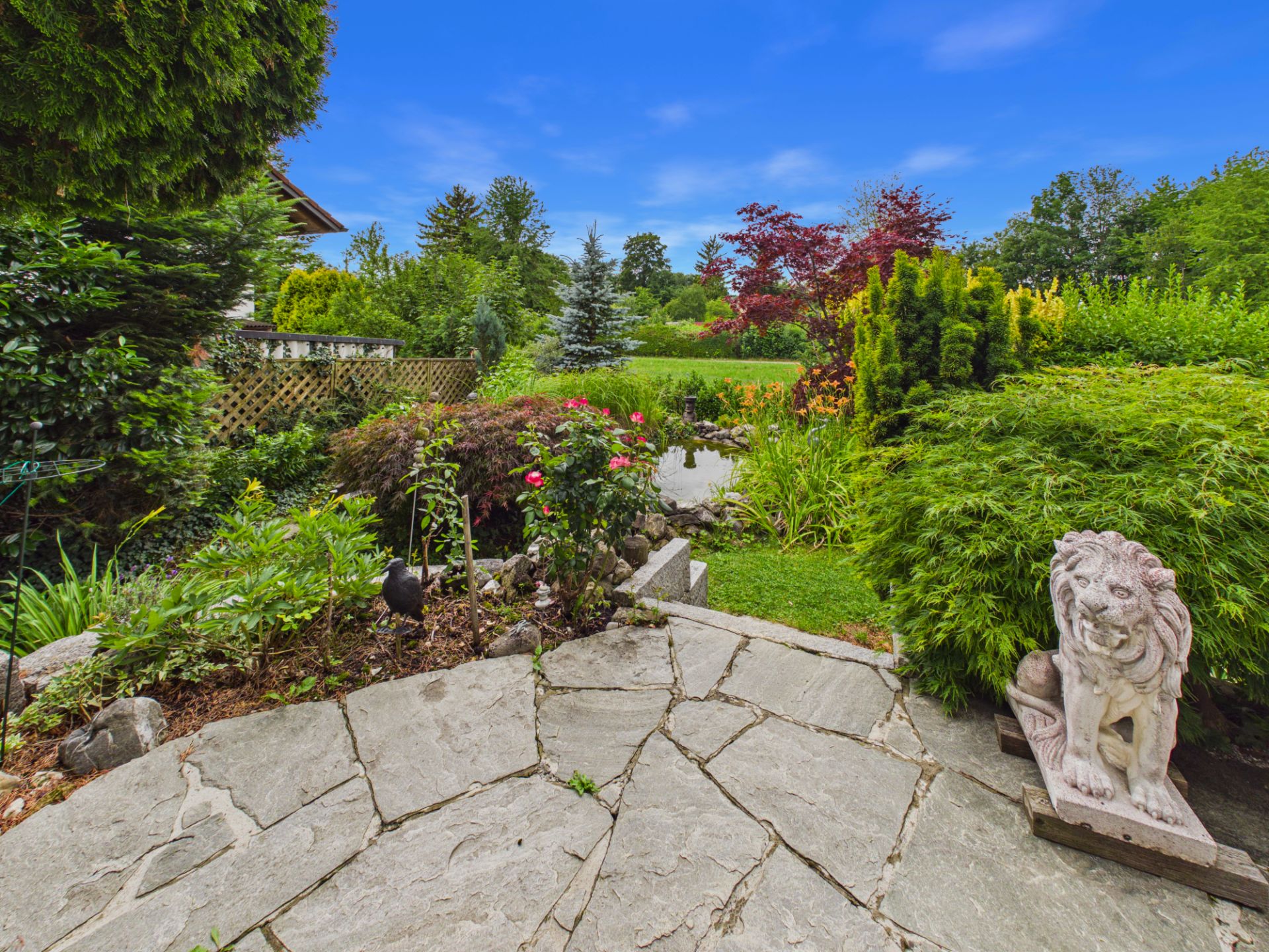 Steingarten mit Löwenskulptur, bunten Blumen und grünem Rasen im Hintergrund.