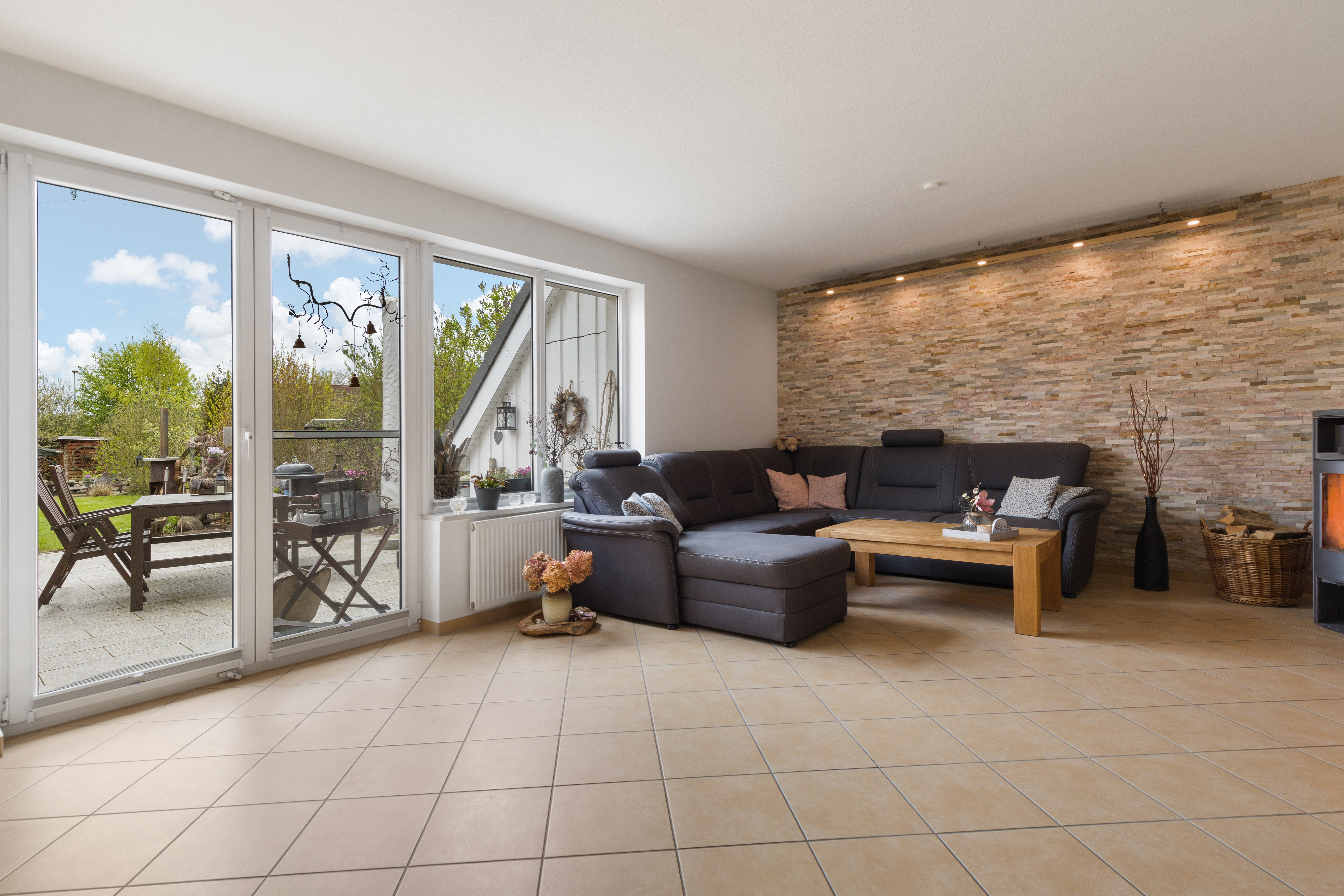 Helles Wohnzimmer mit Ecksofa, Holztisch und Zugang zur Terrasse mit Gartenmöbeln.