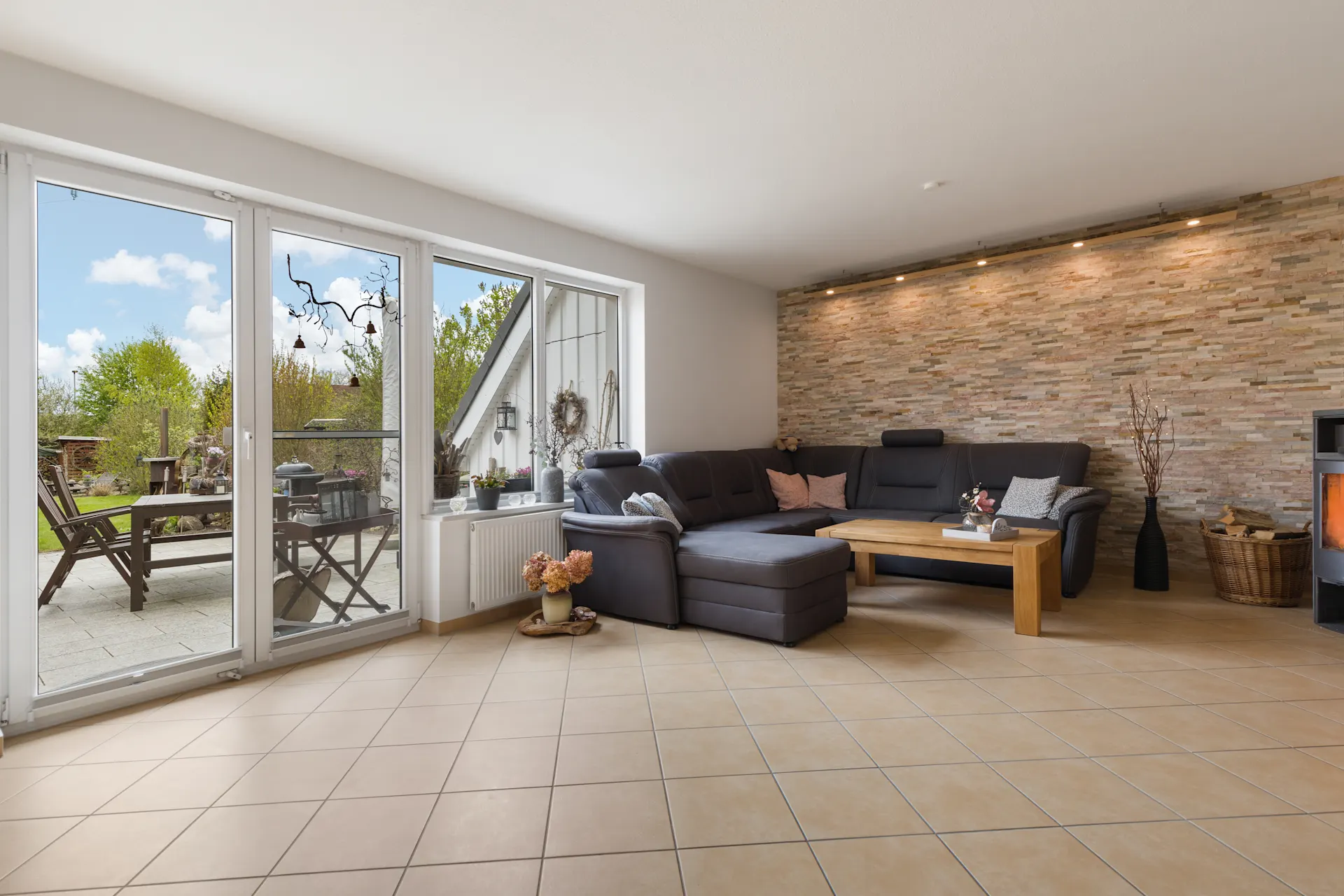 Helles Wohnzimmer mit Ecksofa, Holztisch und Zugang zur Terrasse mit Gartenmöbeln.