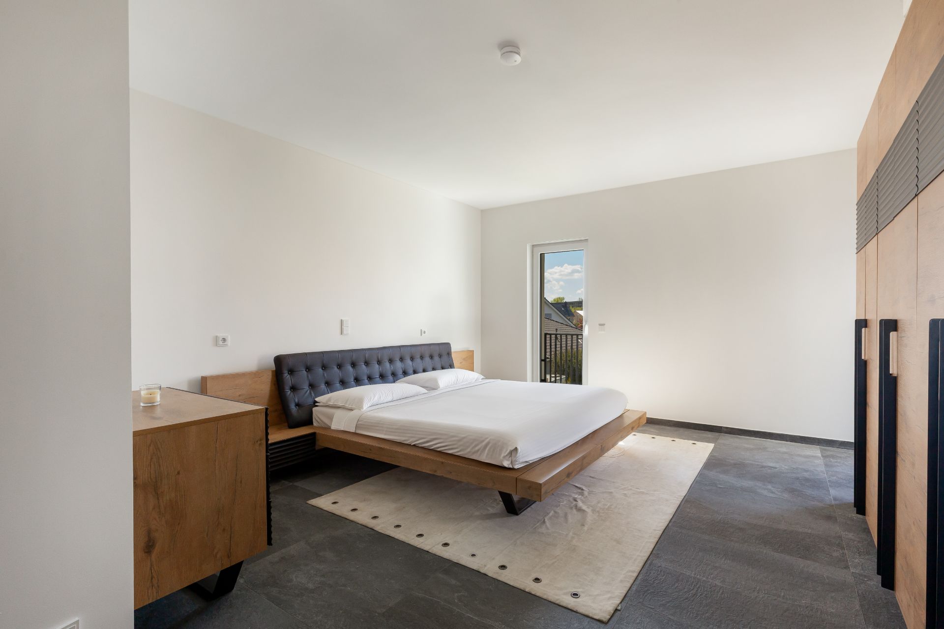 Modernes Schlafzimmer mit Doppelbett, Nachttischen, Teppich und großem Einbauschrank.