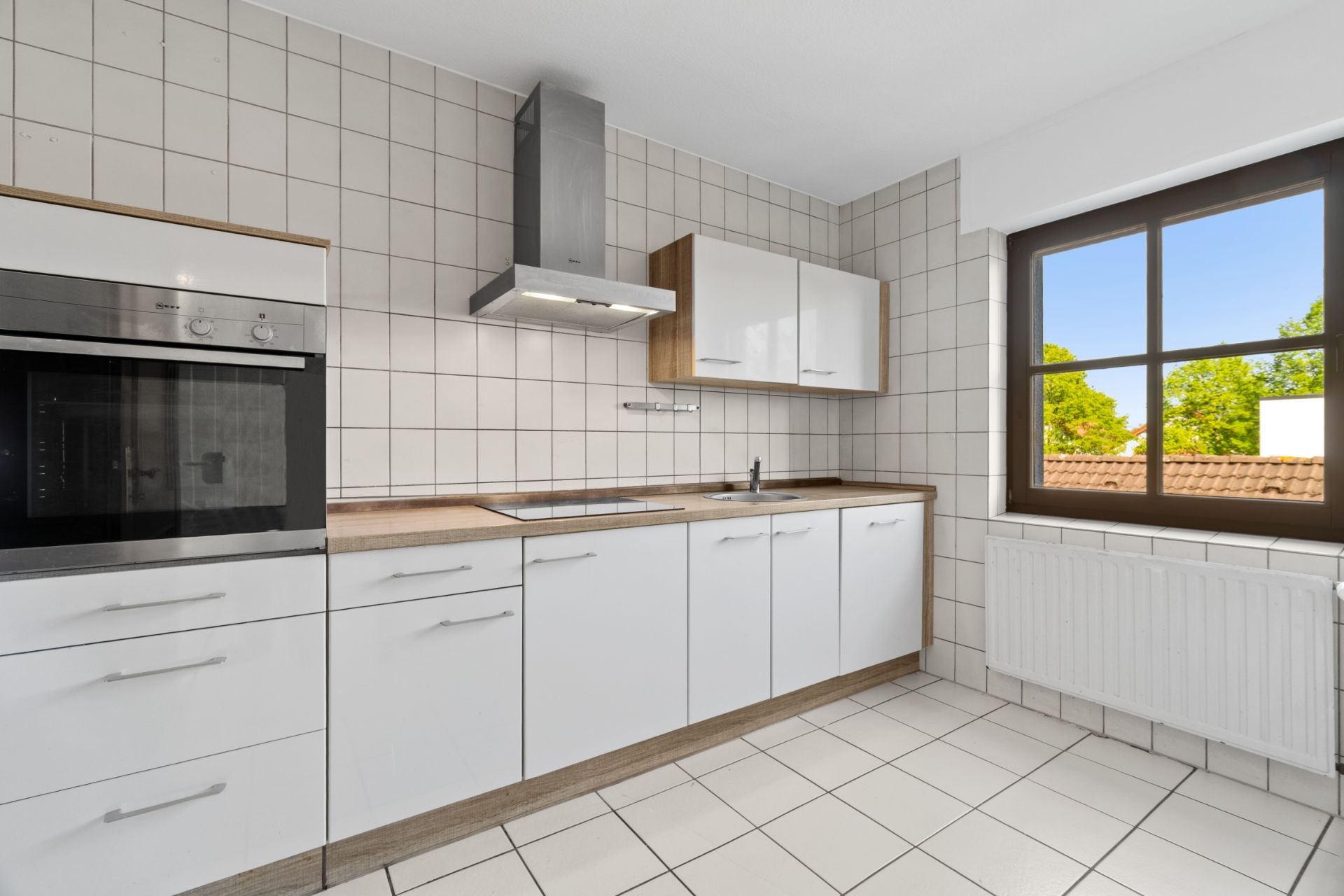 Moderne, helle Küche mit weißen Schränken, Backofen, Herd, Fenster und Heizung.