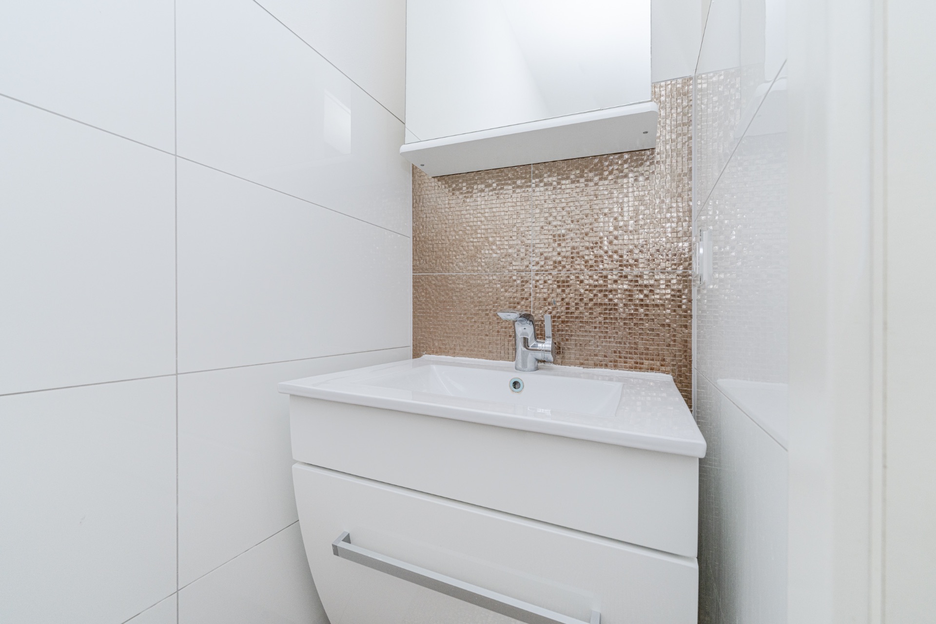 Modernes kleines Waschbecken mit weißem Unterschrank und goldener Mosaikfliese an der Wand.