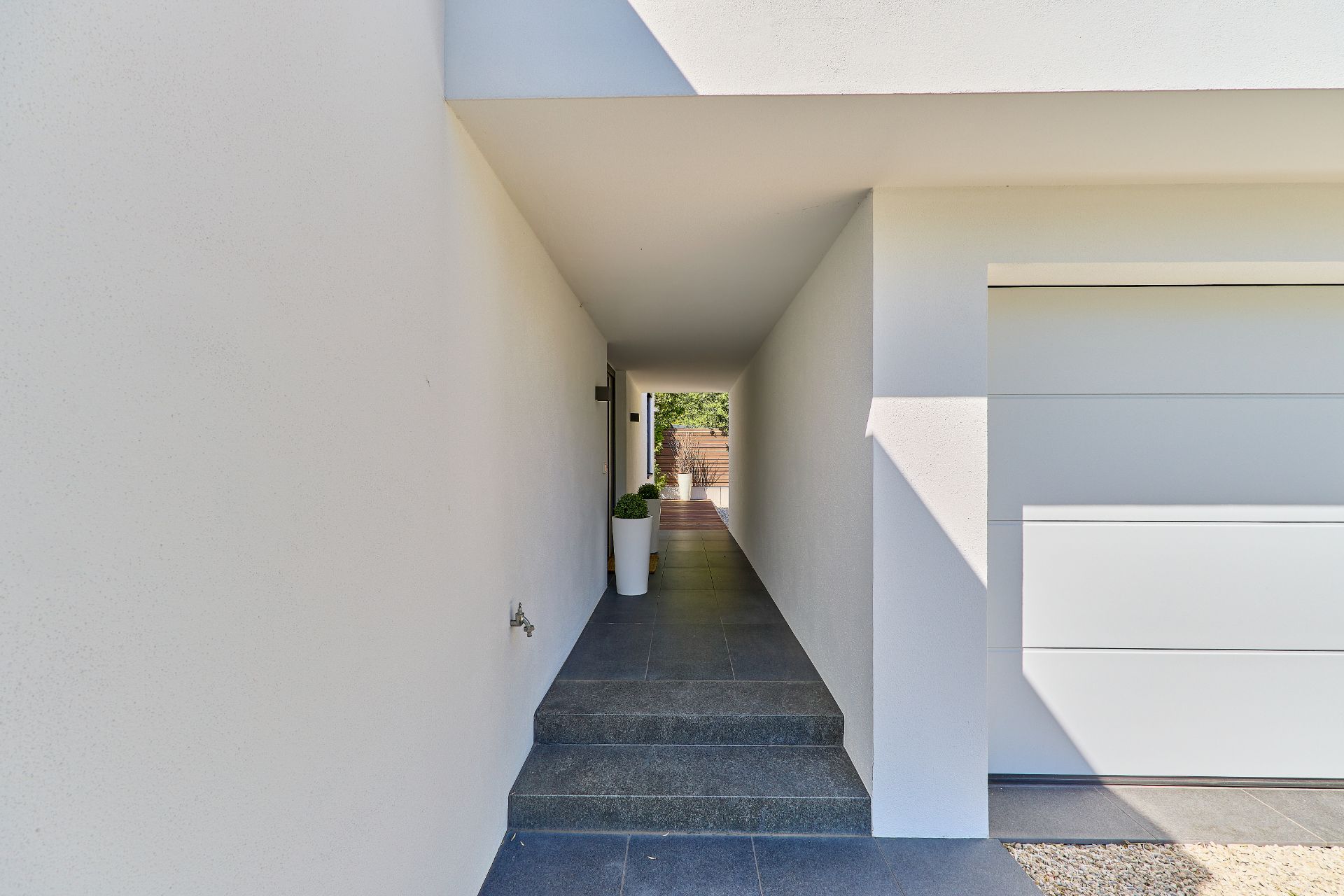 Überdachter Eingangsbereich mit Treppe und zwei weißen Blumentöpfen an der Wand.