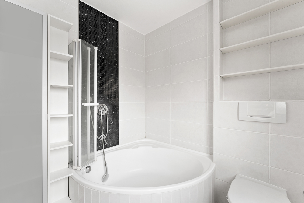 Modernes Badezimmer mit runder Badewanne, Duschwand, weißen Regalen und schwarzen Mosaikfliesen.