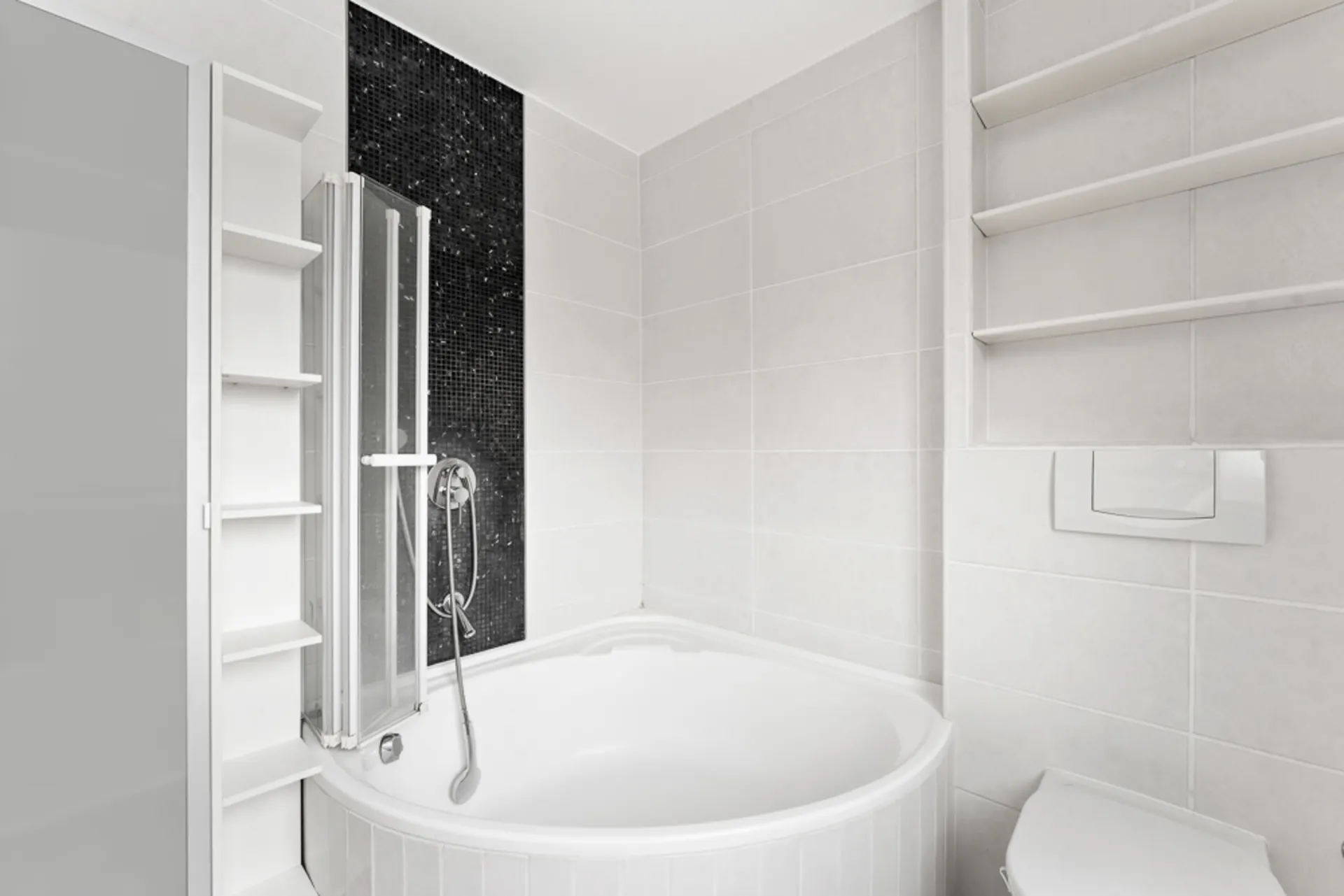 Modernes Badezimmer mit runder Badewanne, Duschwand, weißen Regalen und schwarzen Mosaikfliesen.