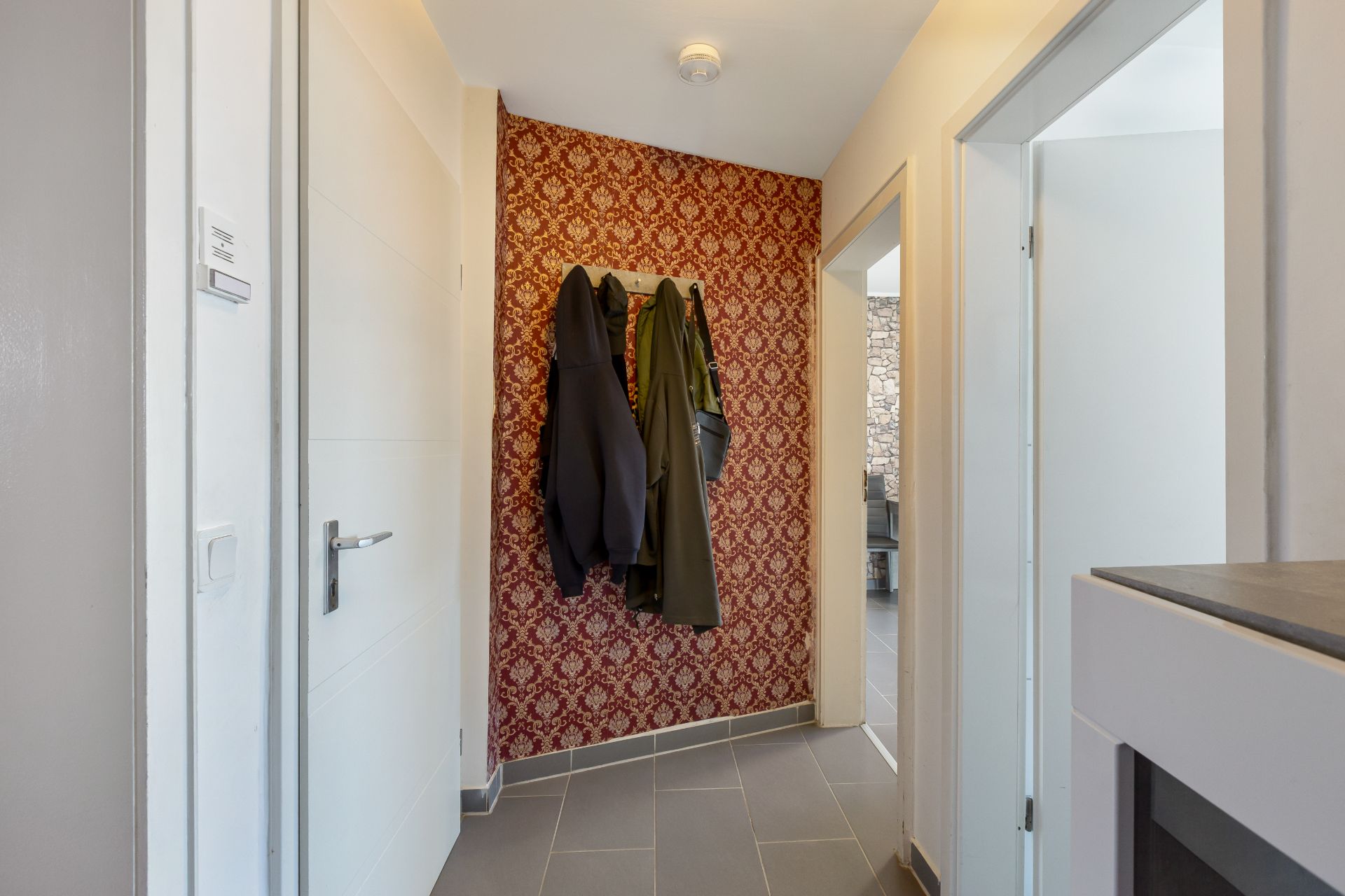 Flur mit roter gemusterter Tapete, Garderobe und zwei Jacken an der Wand.