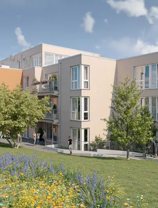 Mehrfamilienhaus mit Balkonen, Bäumen und Blumenwiese im Vordergrund bei Tageslicht.