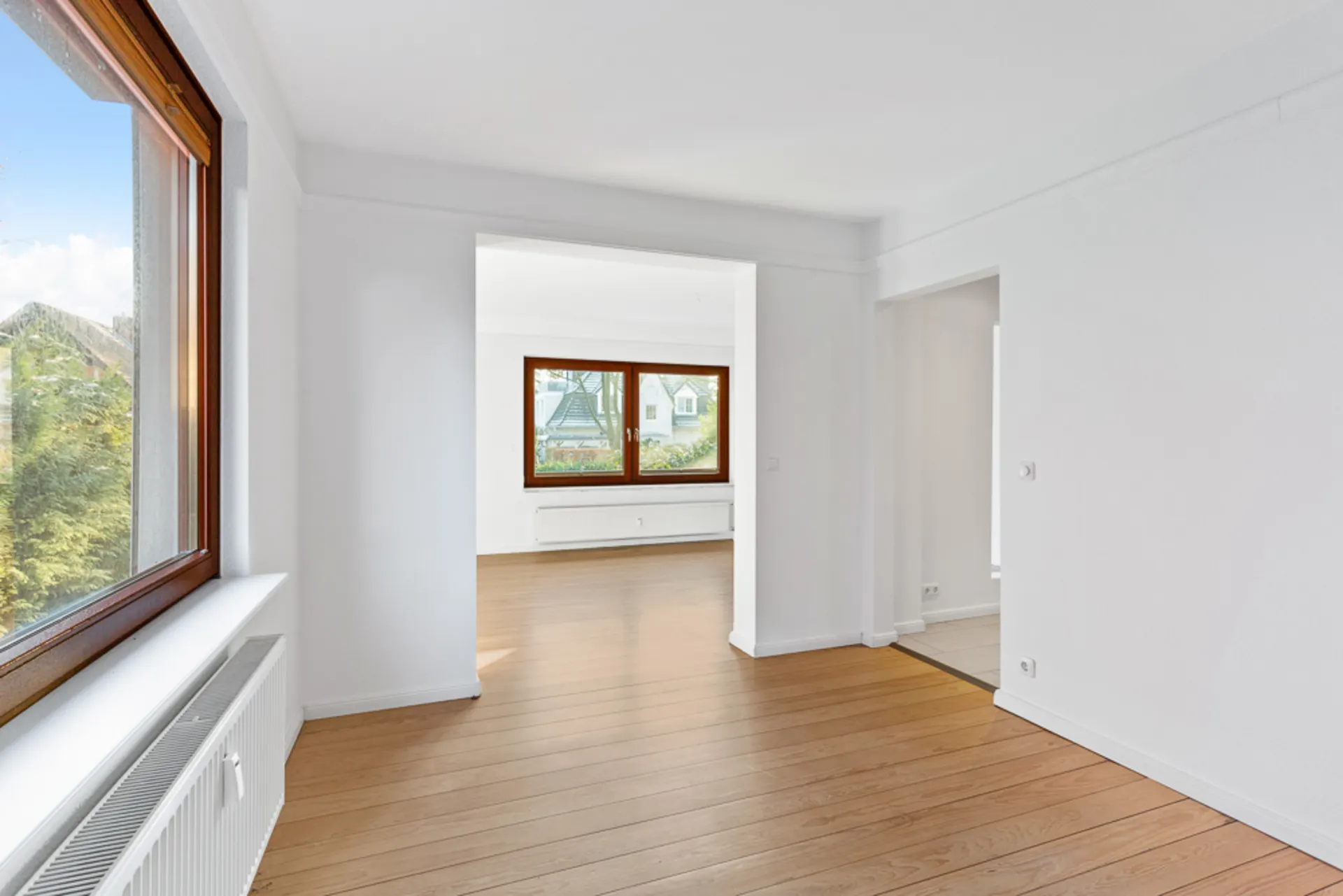Heller Raum mit großen Fenstern, weiß gestrichenen Wänden und Holzfußboden.