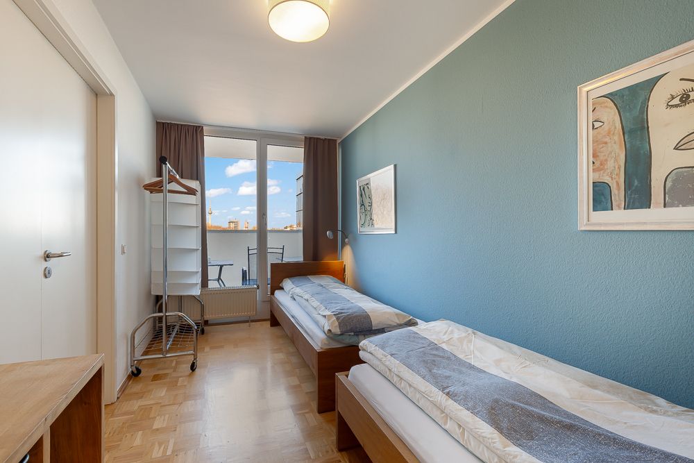 Schlafzimmer mit zwei Einzelbetten, blau gestrichener Wand und Zugang zu einem Balkon mit Stühlen.