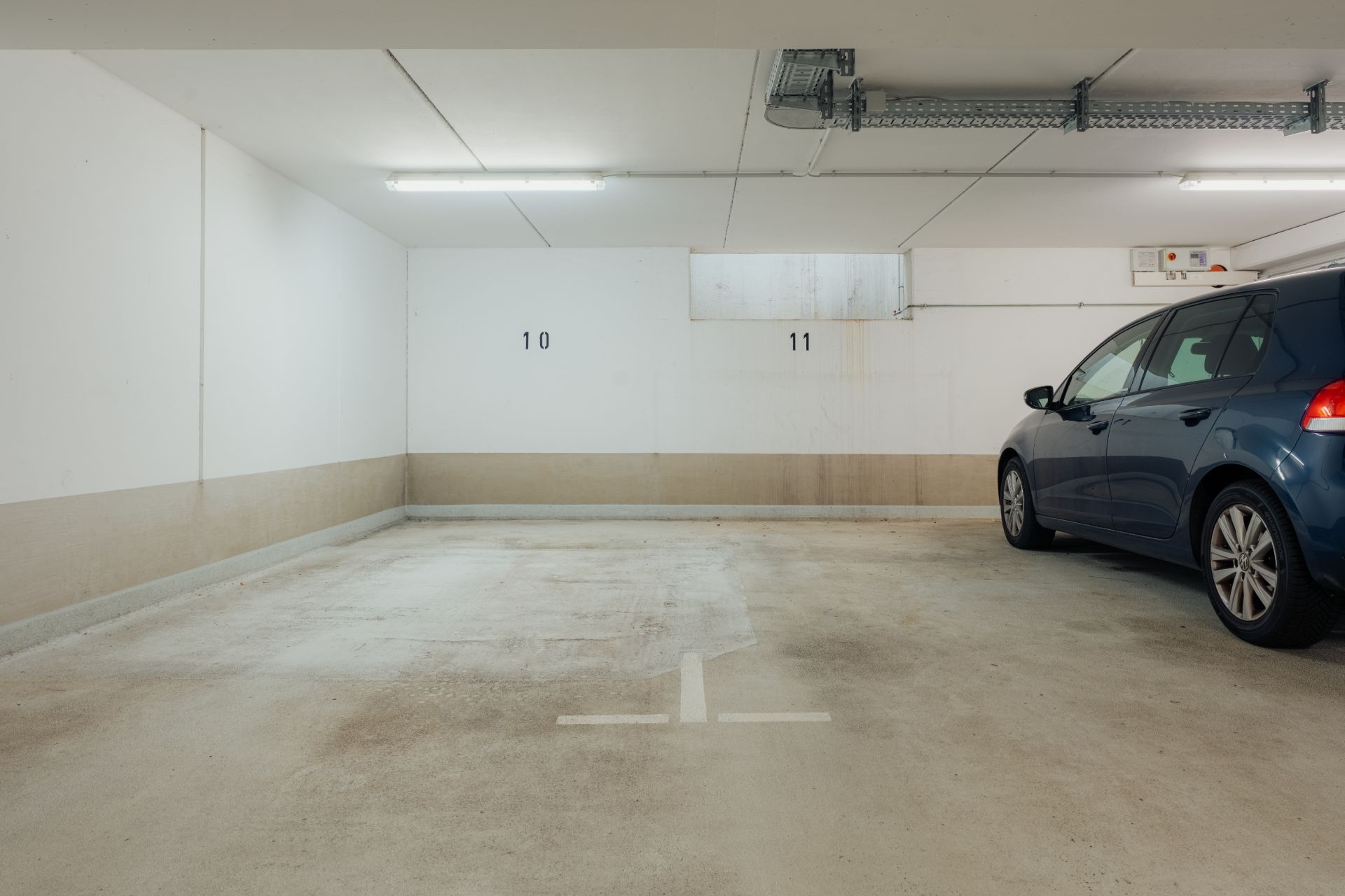 Tiefgaragenstellplatz mit weißer Wand, Nummern 10 und 11, und einem blauen Auto rechts.