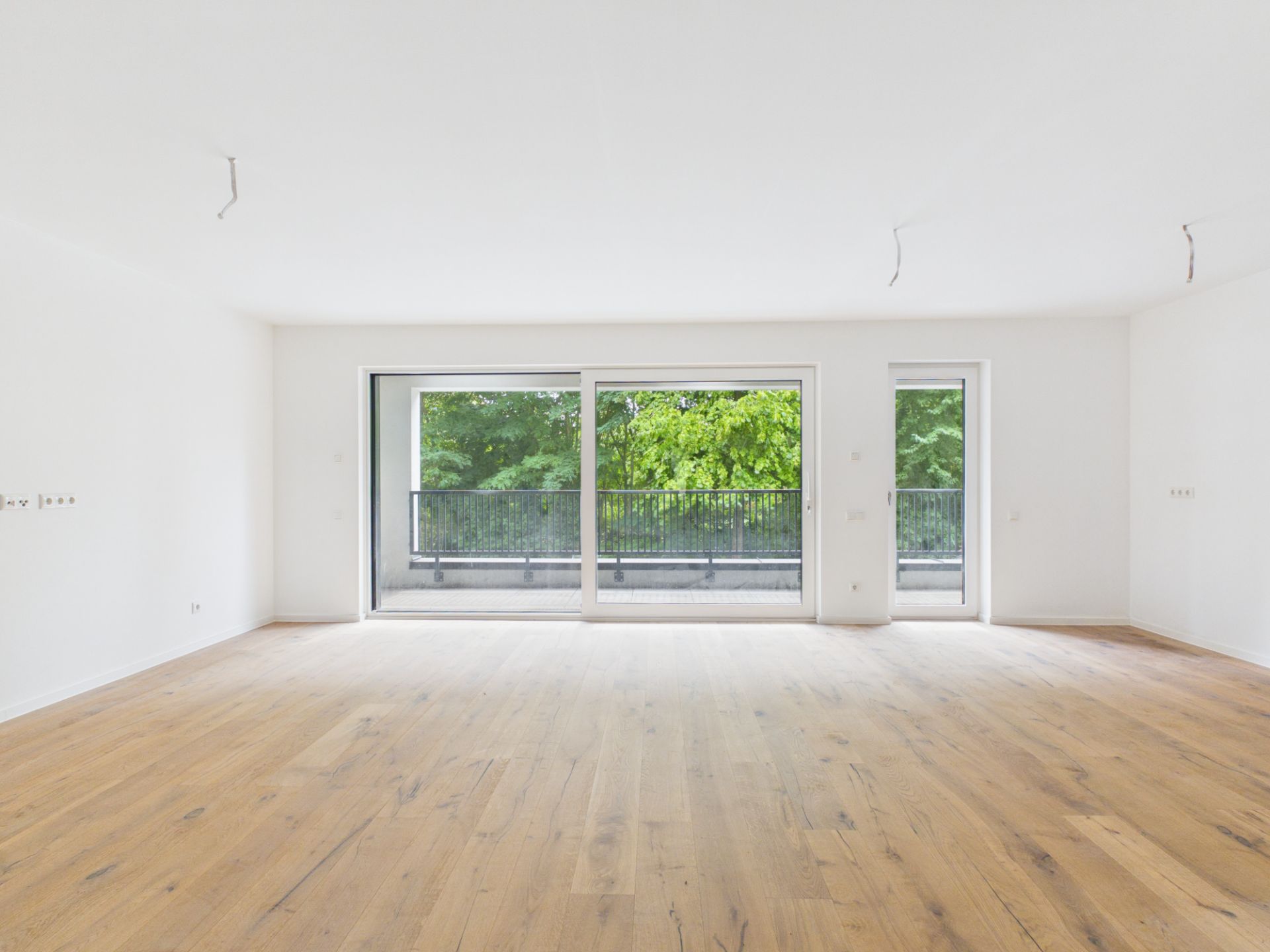Helles, leeres Wohnzimmer mit Parkettboden und großen Fenstern zur Terrasse.