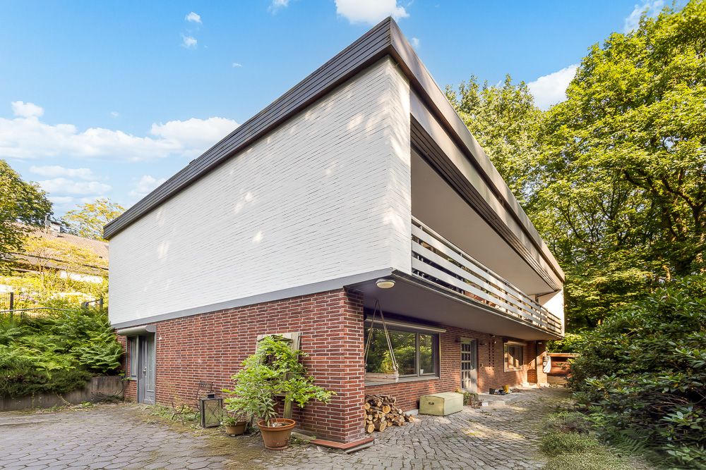 Modernes zweistöckiges Wohnhaus mit Ziegel- und weißer Fassade, großem Balkon und Pflanzen im Vorgarten.