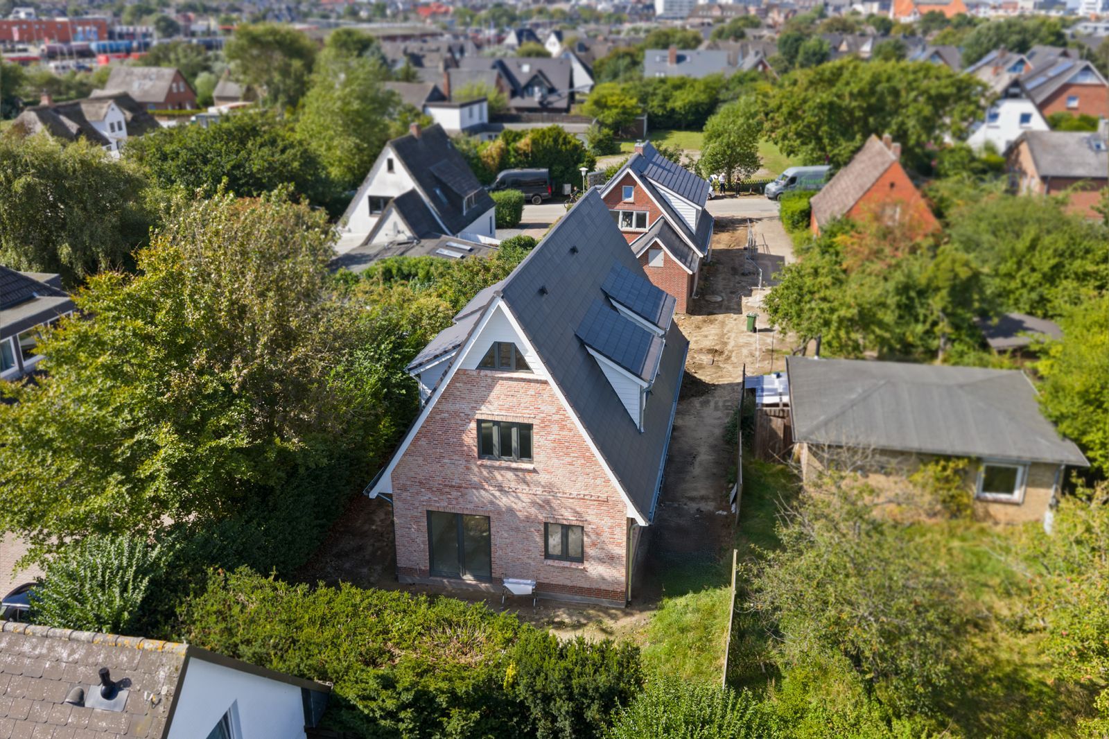Luftaufnahme eines roten Backsteinhauses mit Spitzdach und Garten, umgeben von weiteren Häusern.