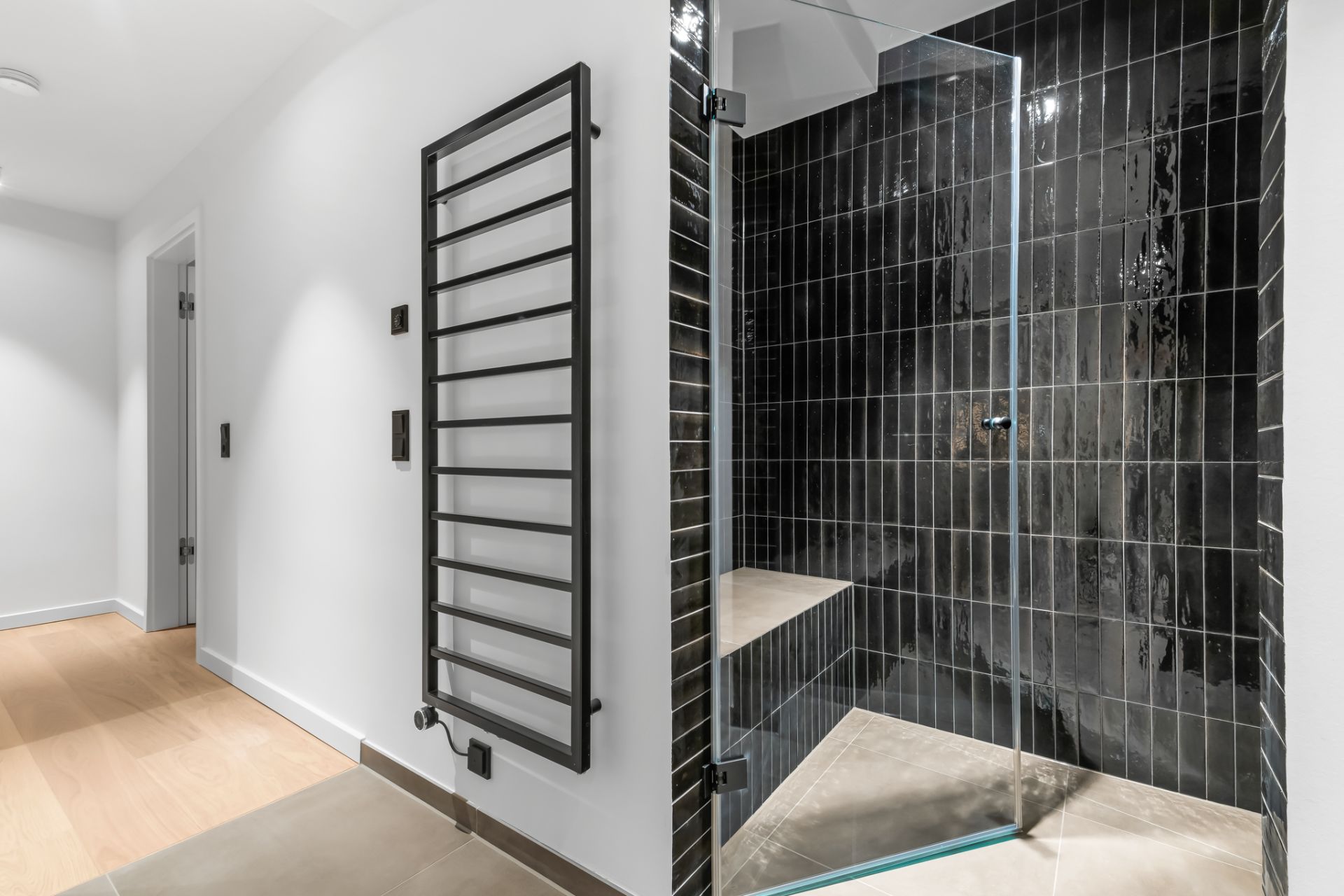 Modernes Badezimmer mit schwarzer gefliester Dusche und Handtuchheizkörper an weißer Wand.