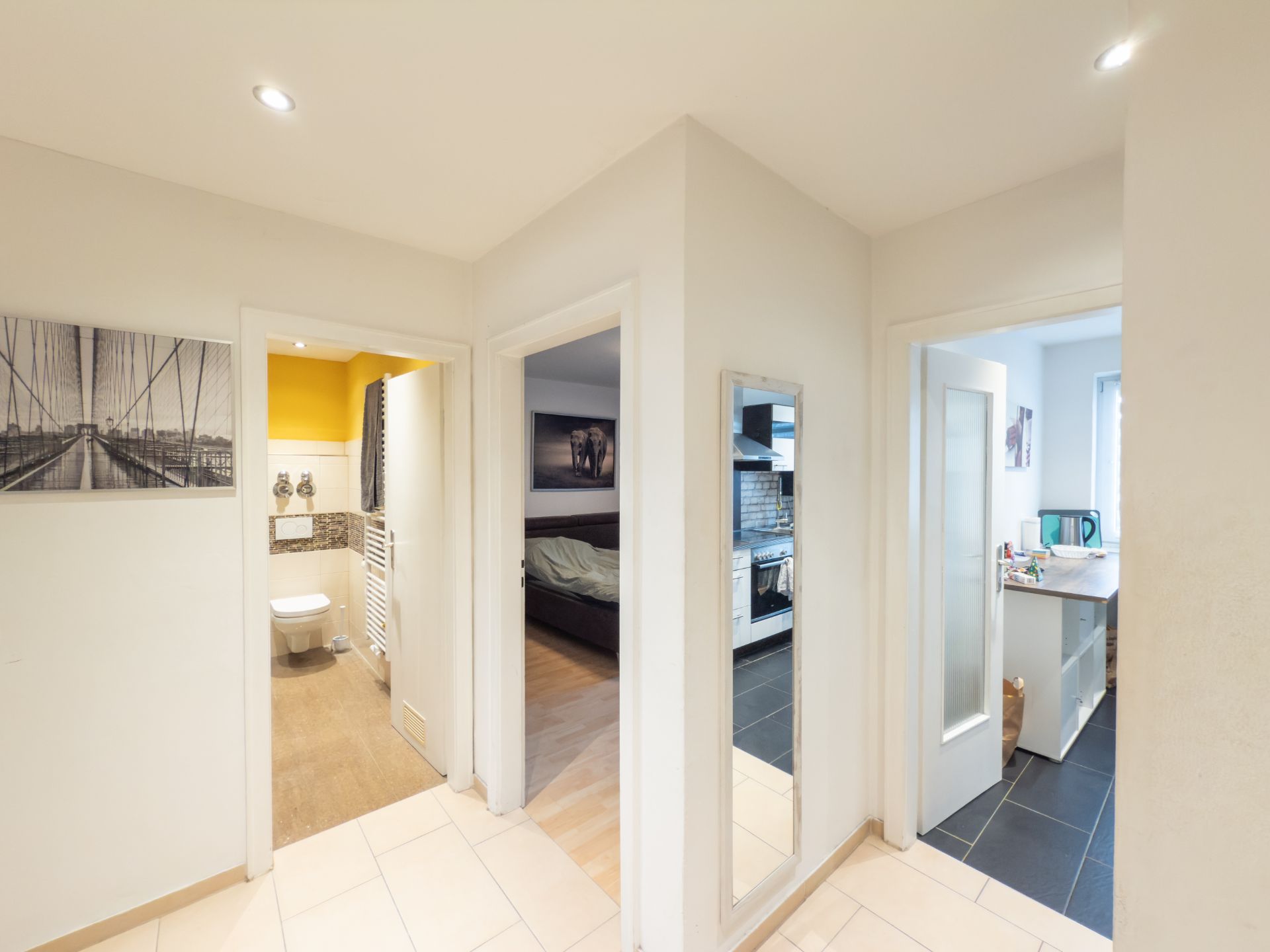 Flur mit Zugang zu Bad, Schlafzimmer und Küche, Wandspiegel und Wandbilder sichtbar.