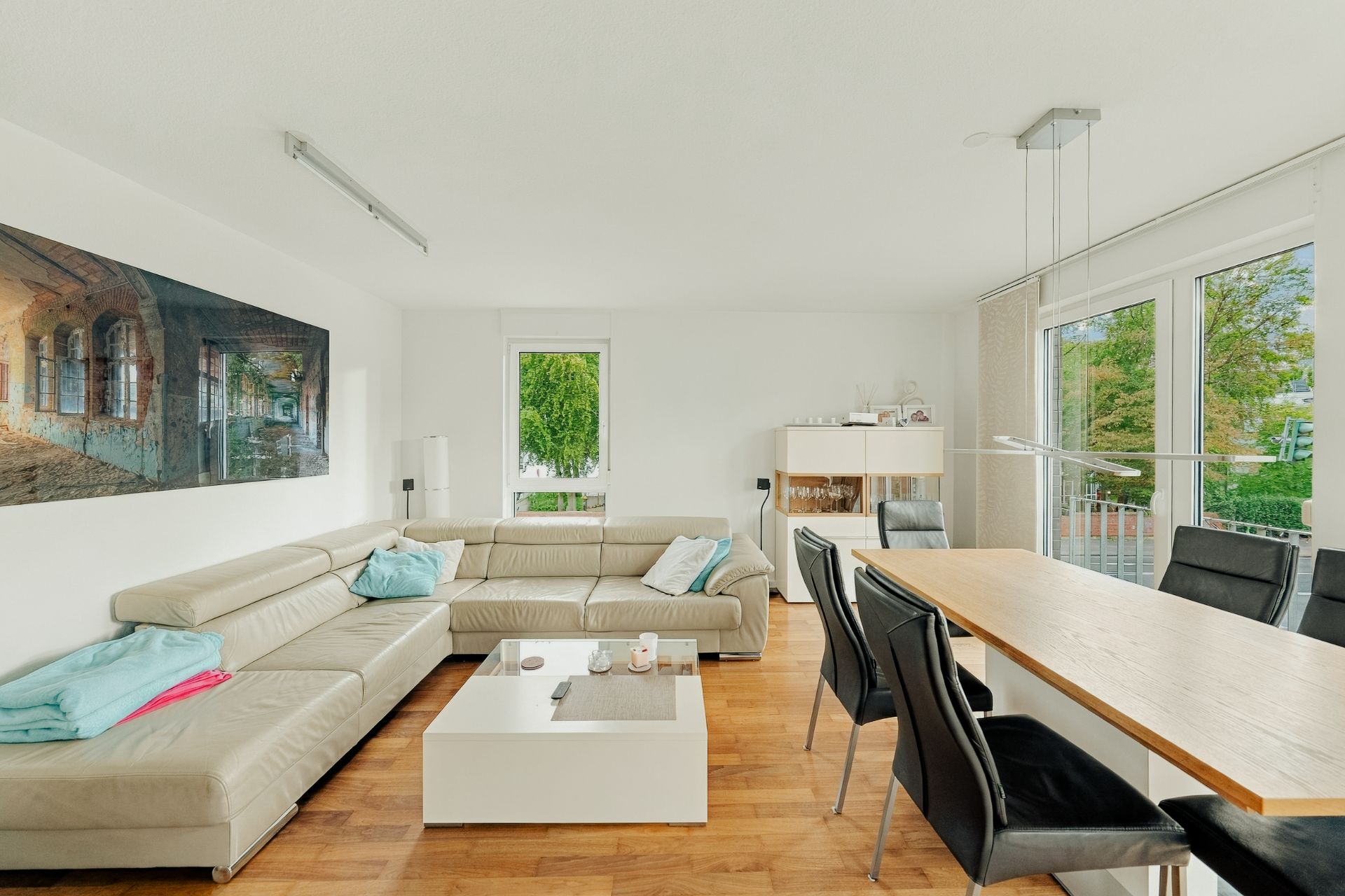 Helles Wohnzimmer mit Ecksofa, Couchtisch, Essbereich und großen Fenstern mit Blick nach draußen.