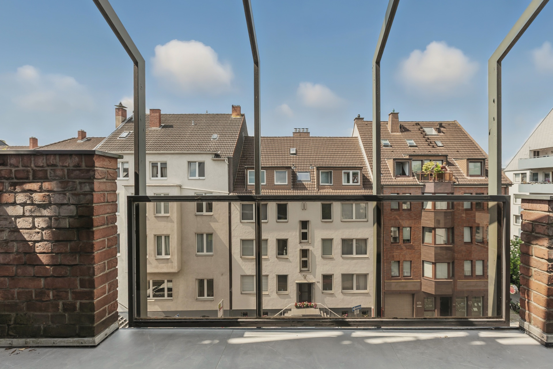 Blick von einem Balkon auf Wohnhäuser mit Ziegel- und hellen Fassaden.
