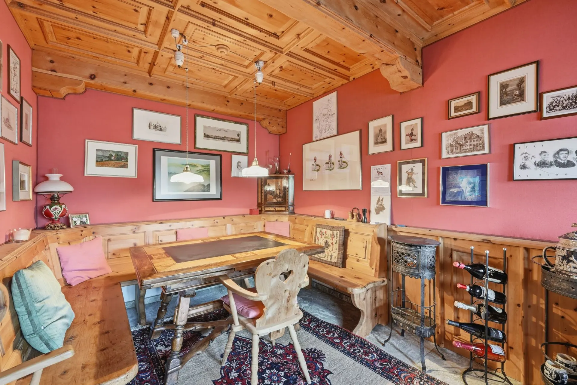 Gemütliches Esszimmer mit Holzbänken, Holztisch, Teppich und vielen Bildern an roten Wänden.